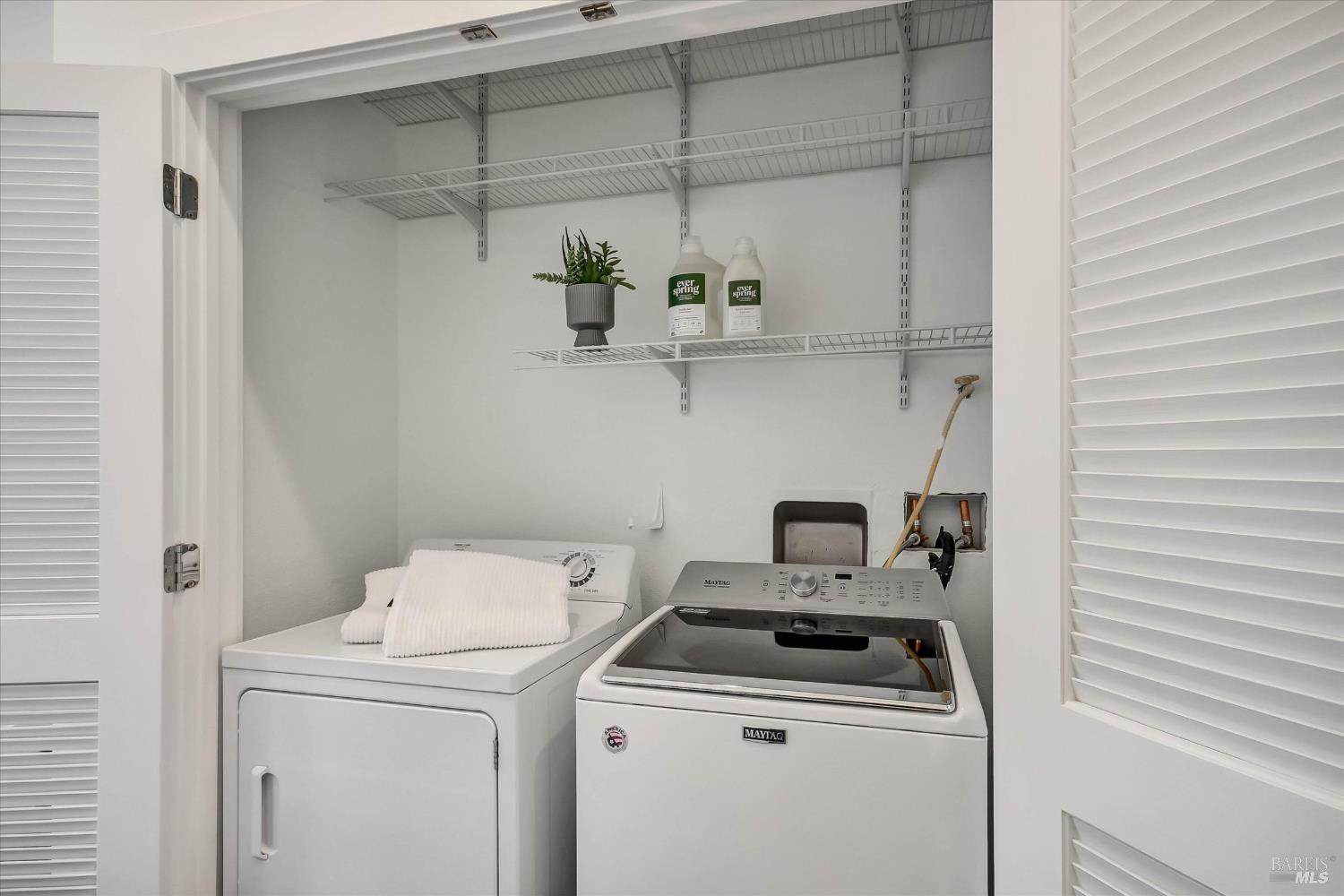 Laundry room with a white Maytag washer and dryer beneath wire shelves.