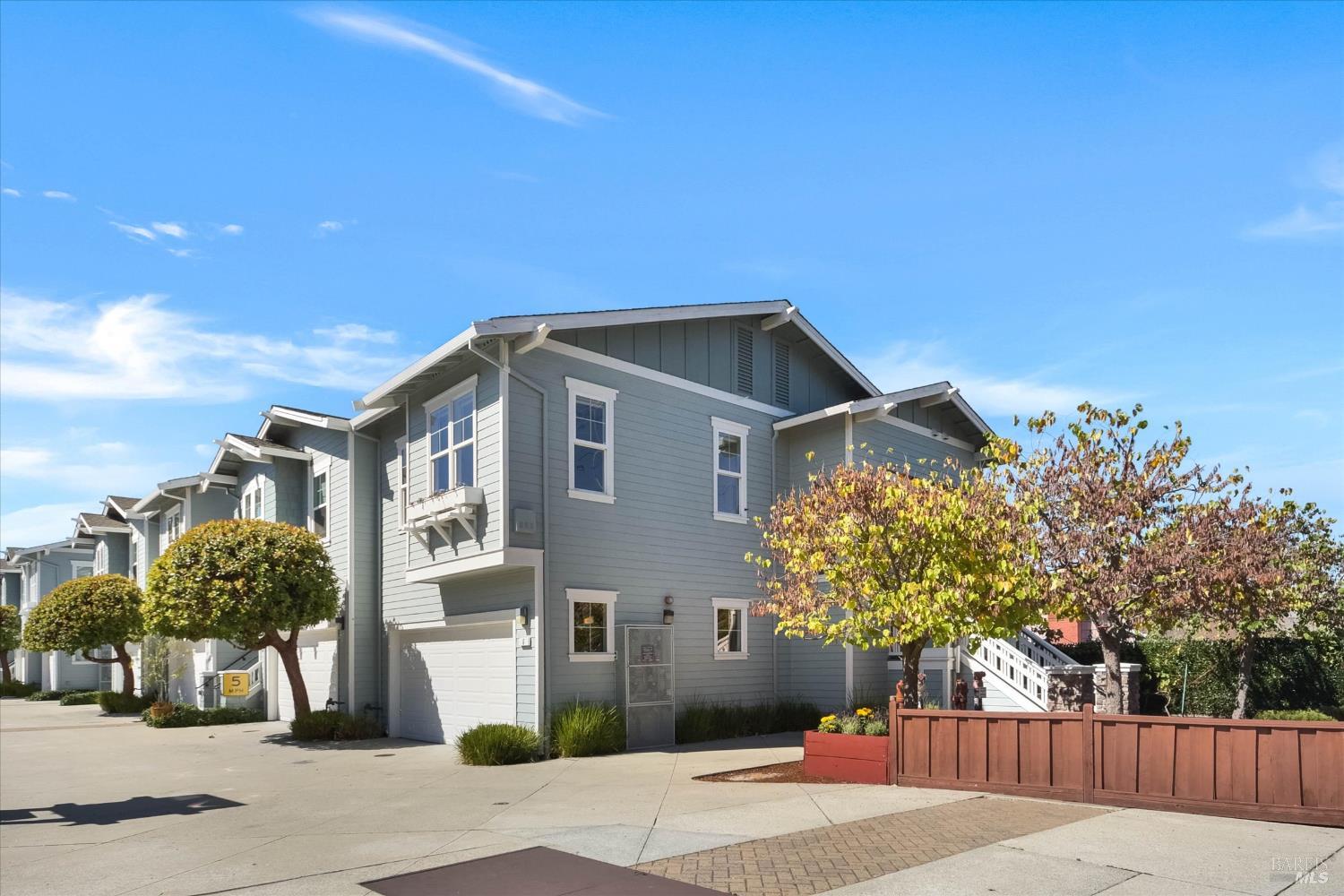 Gray-blue two-story townhouse with a garage, landscaped entry, and red-brown fence.