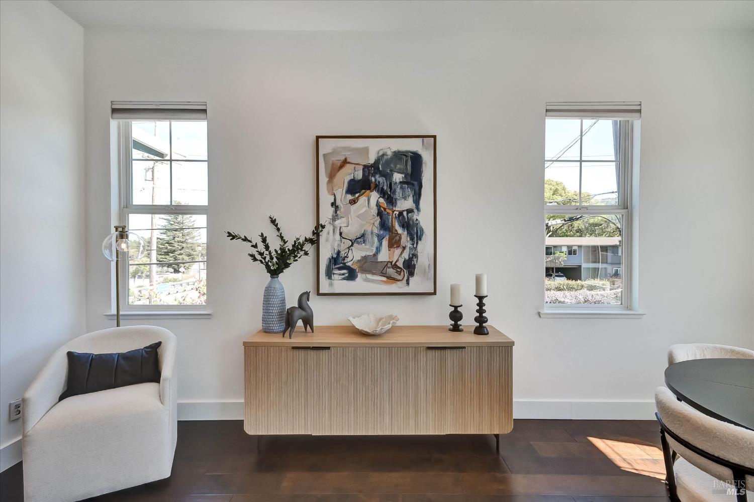 Staged dining area with a ribbed wood console, abstract artwork, and two sunlit windows.