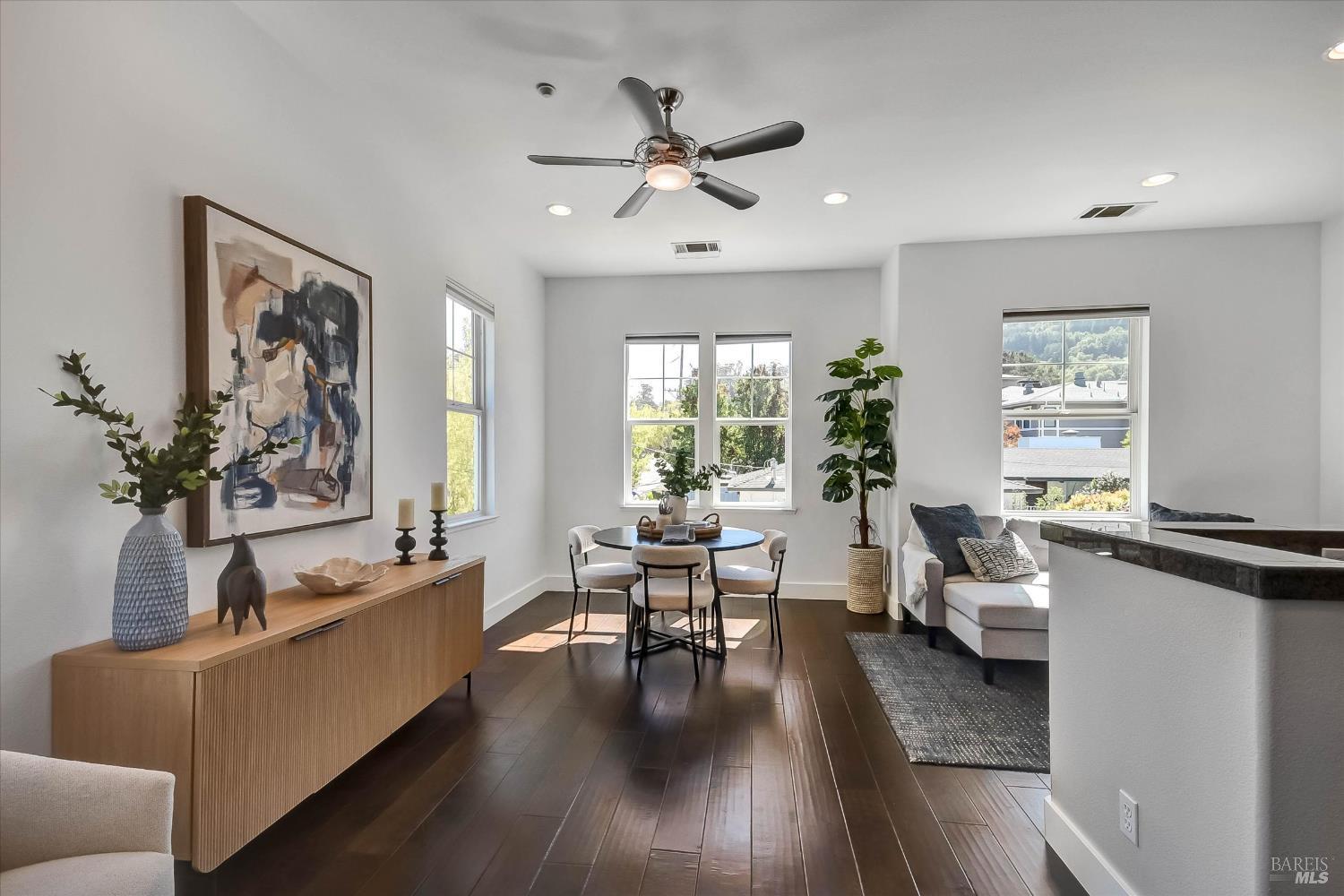 Open-plan dining and living area with a round table, white sofa, and wooded hillside views.