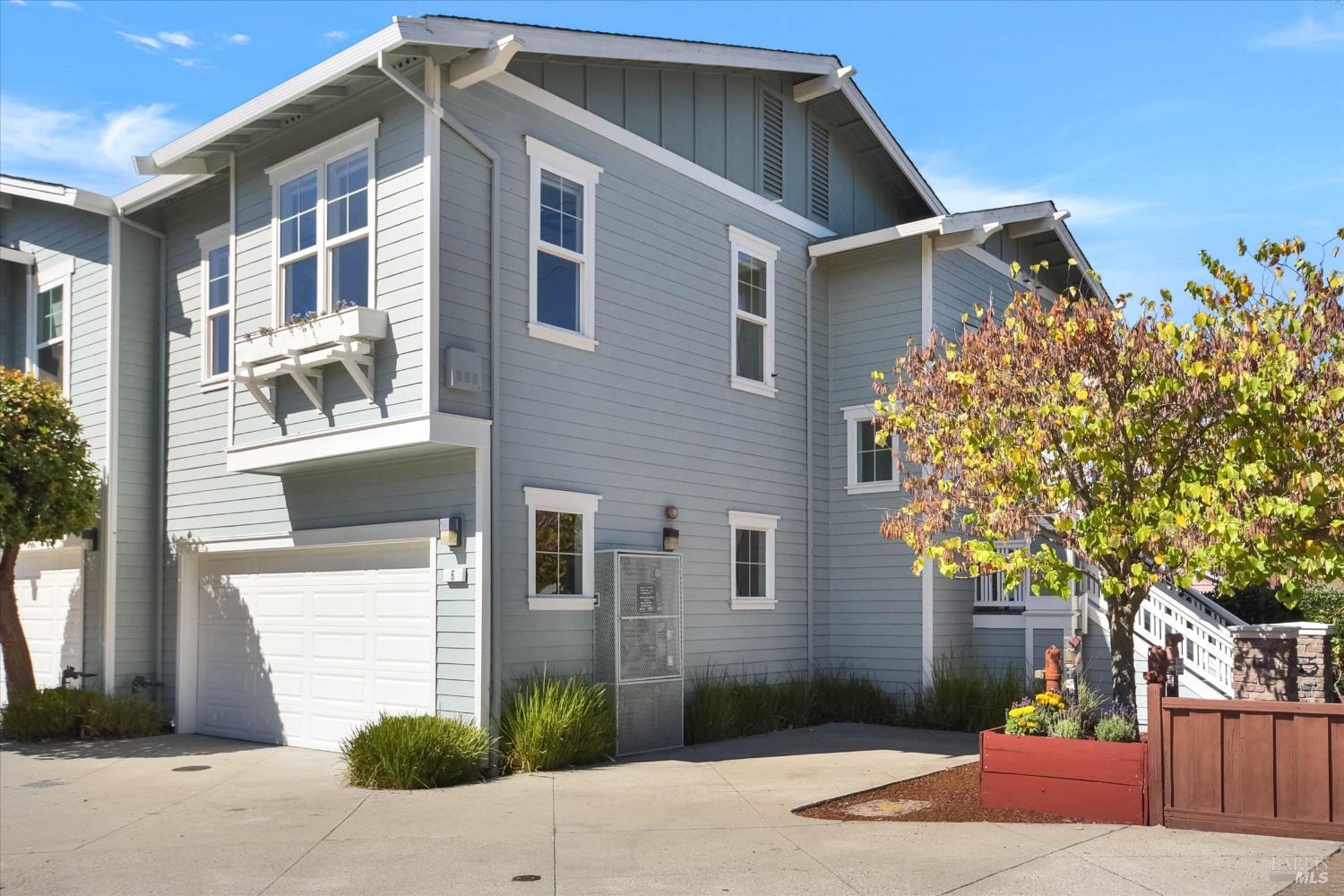 Blue-gray multi-story home with white trim, an attached garage, balcony, and autumn-colored tree.