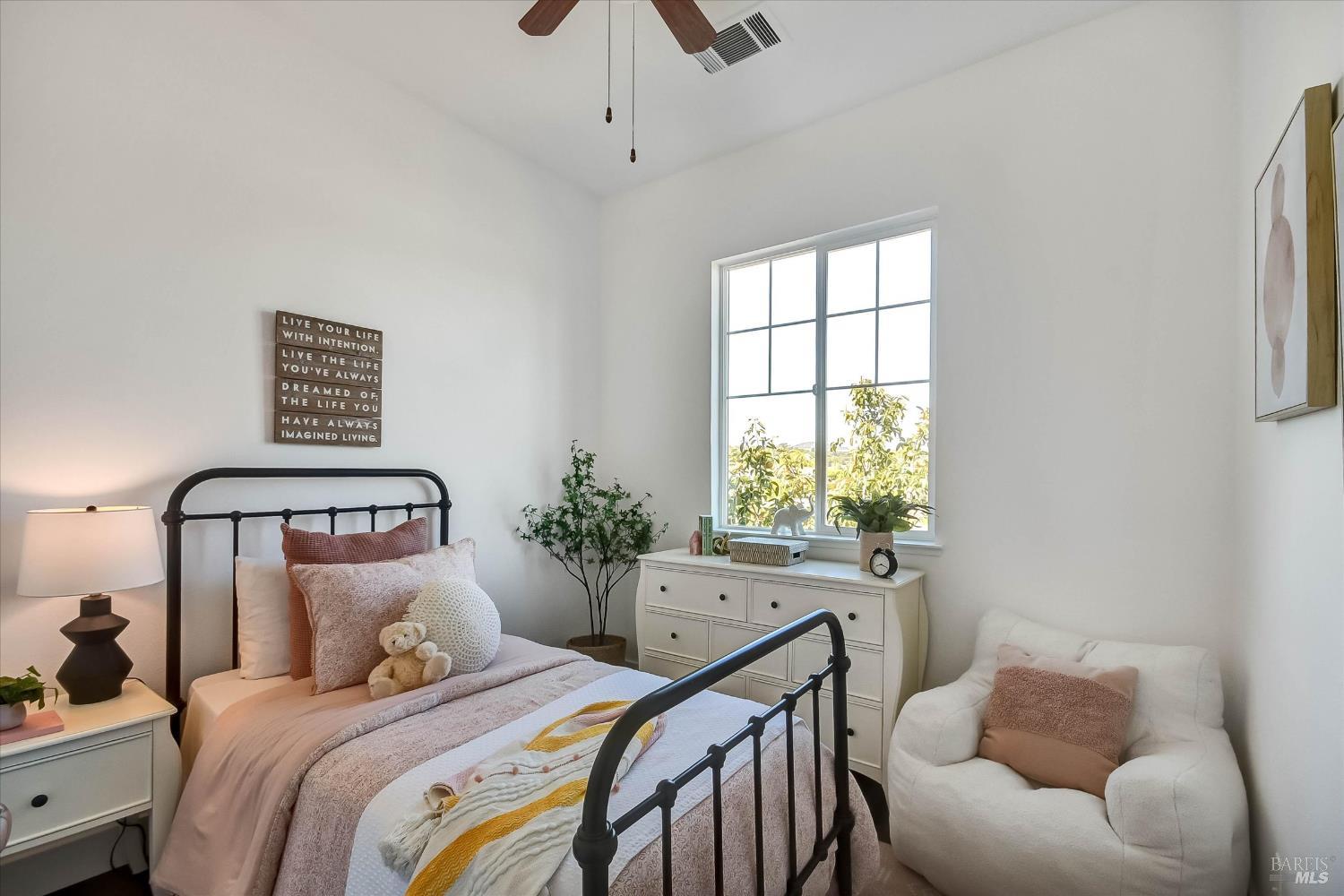 Staged bedroom with a black metal bed, blush bedding, a bright divided-pane window, and a white armchair.
