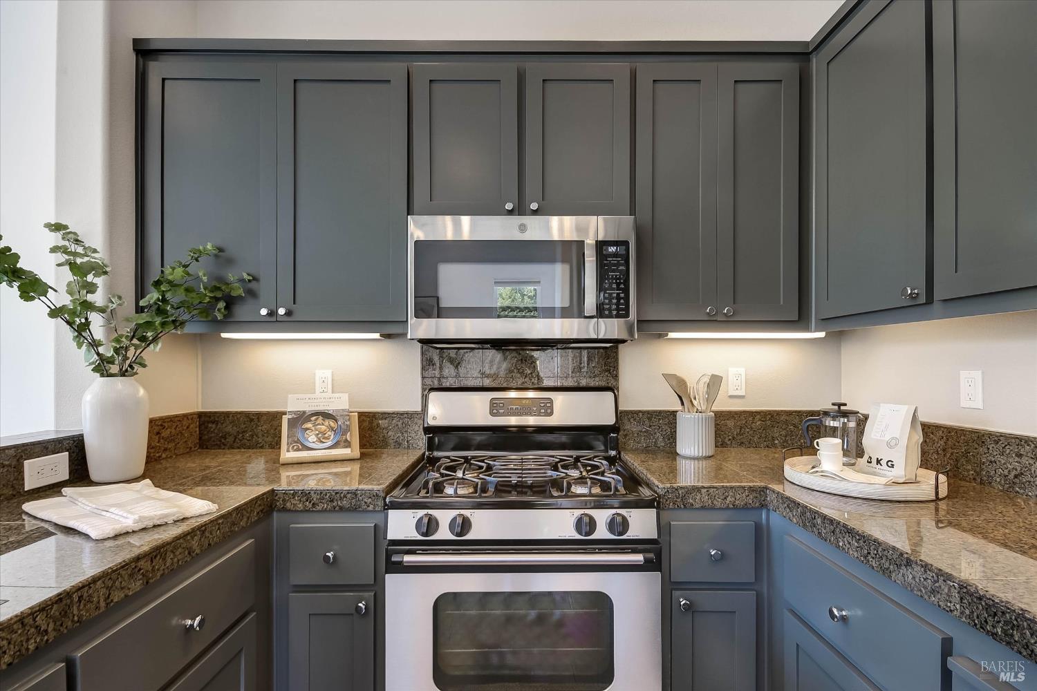Kitchen with dark paneled cabinets, stone counters, and a stainless gas range beneath a built-in microwave.