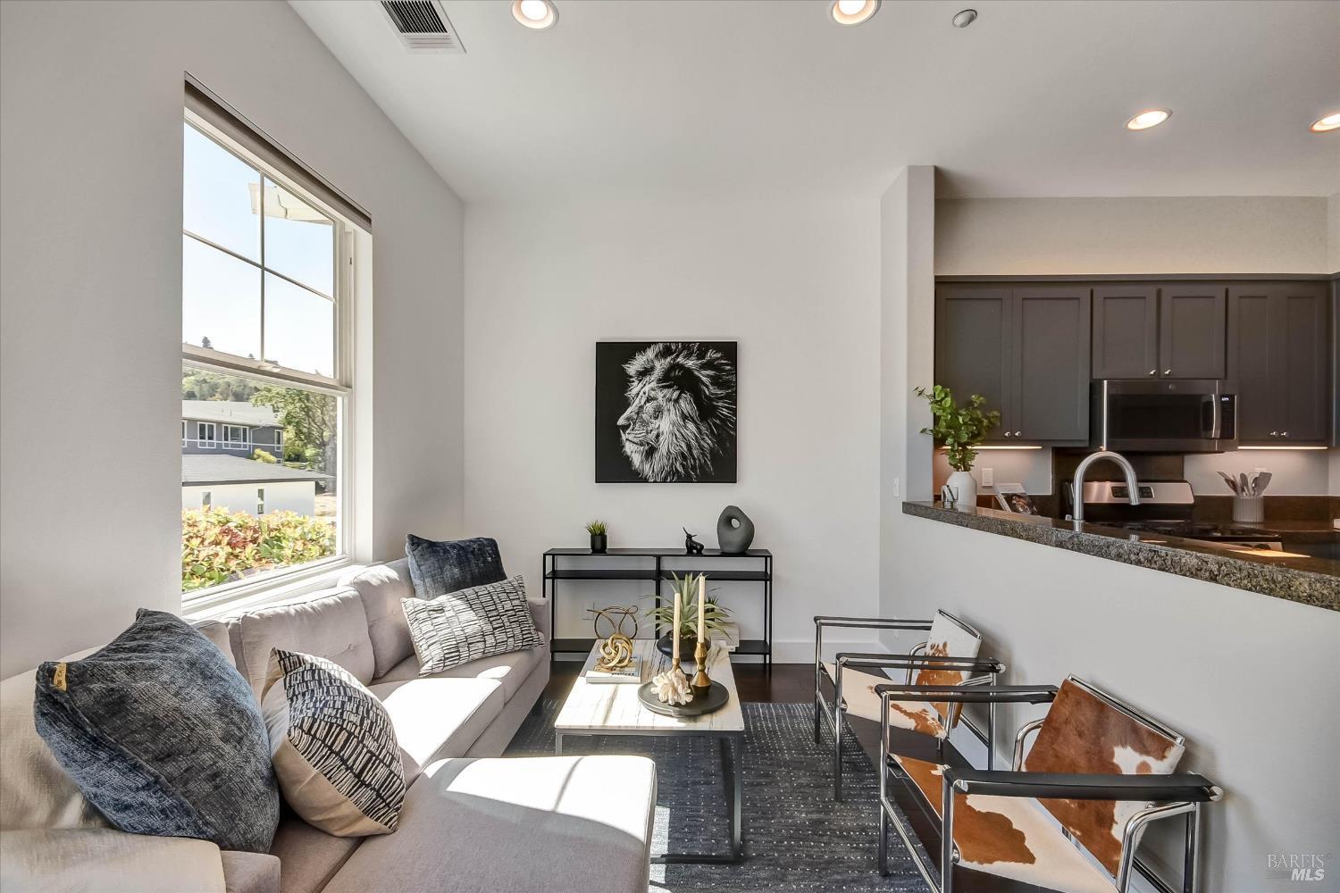 Furnished living room with a large window, lion portrait, and open kitchen.