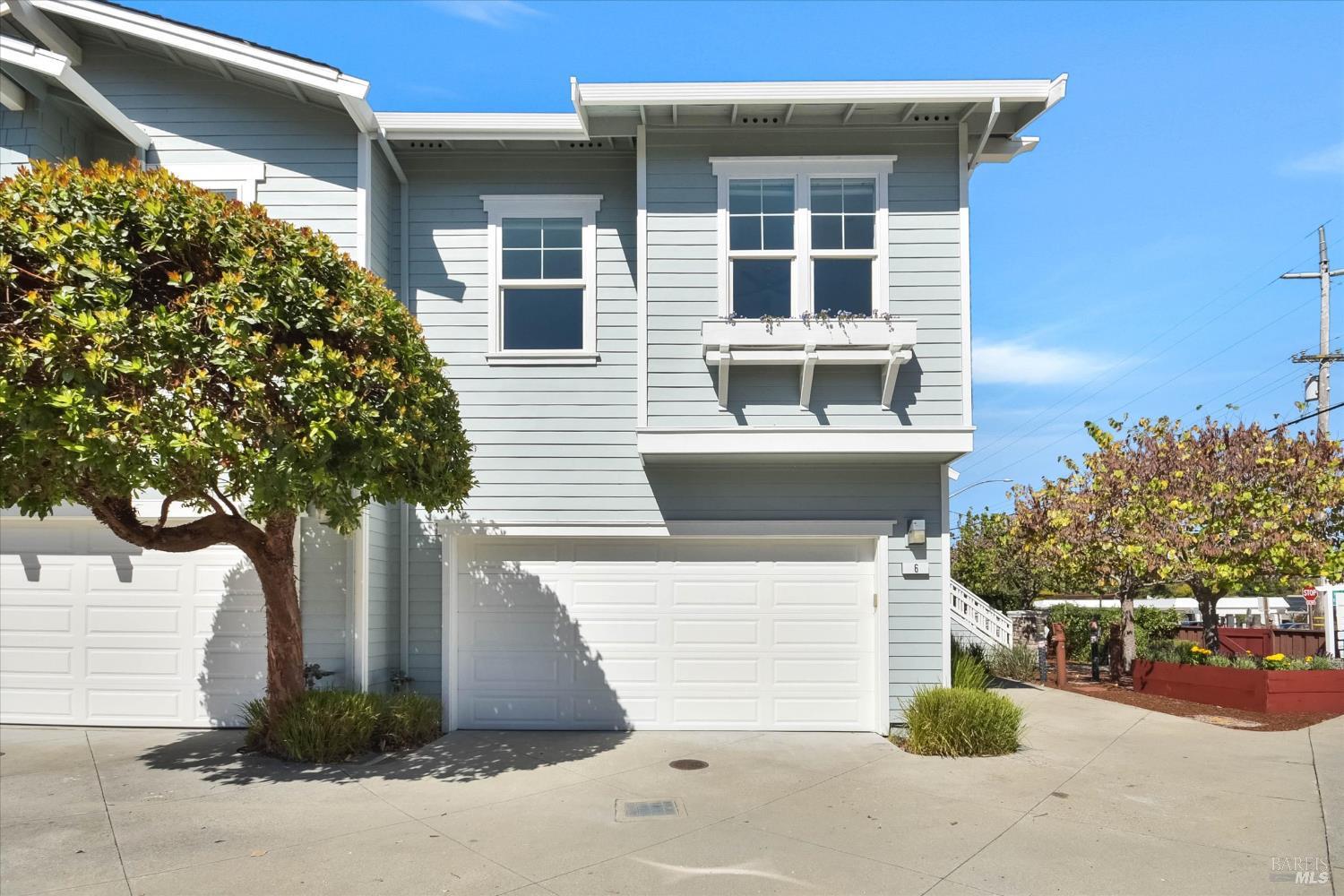 Blue-gray two-story home with white trim, garage doors, and a leafy tree in front.