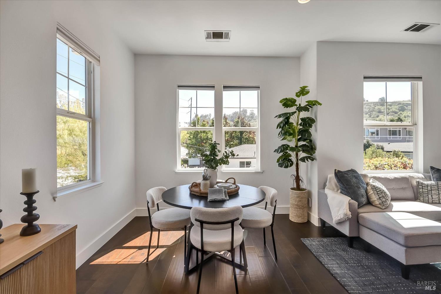 Staged living and dining area with a round table, gray sectional, and large hillside-facing windows.