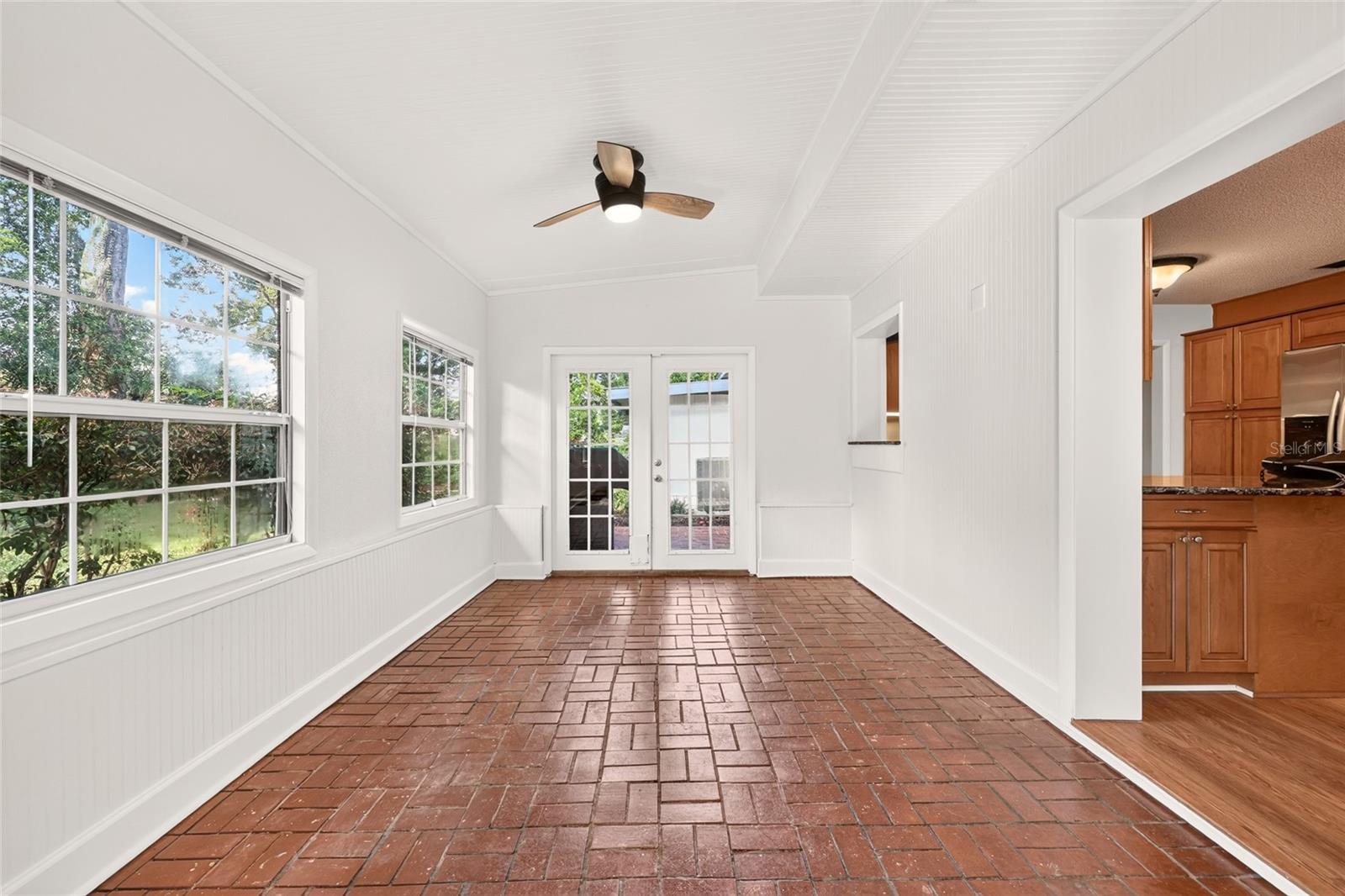 Enclosed sunroom with brick-pattern tile flooring, large windows, and glass double doors.