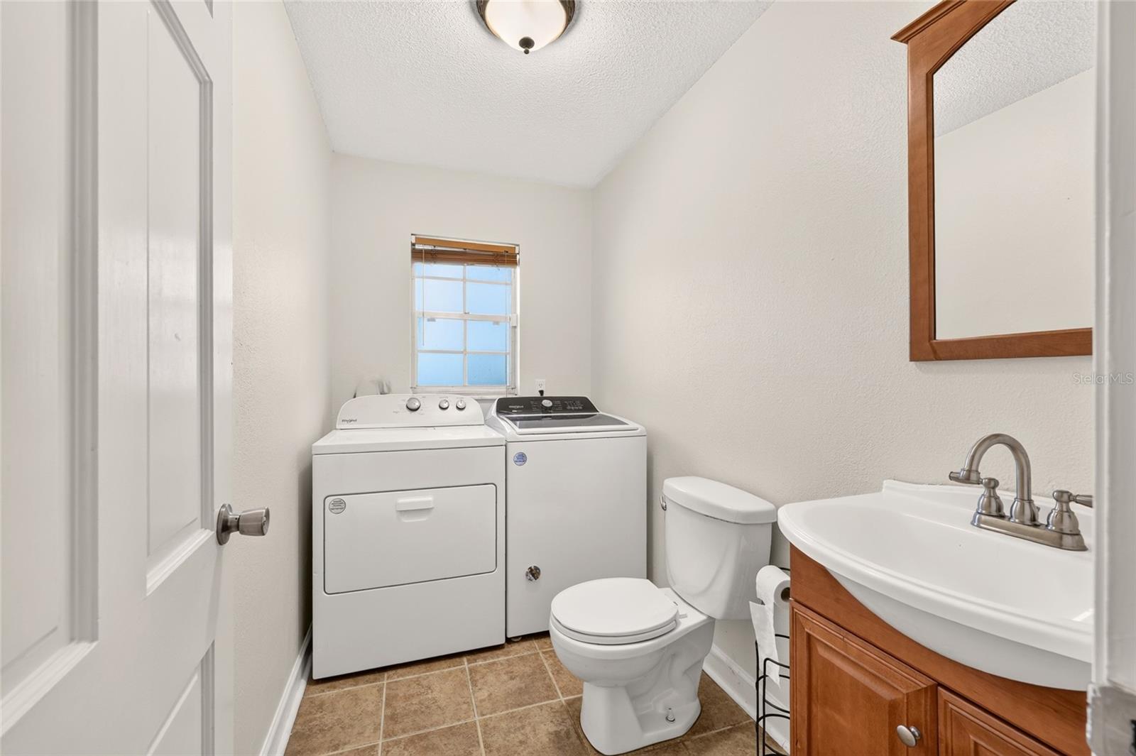 Bathroom with washer and dryer, toilet, and white sink vanity with wood cabinetry.