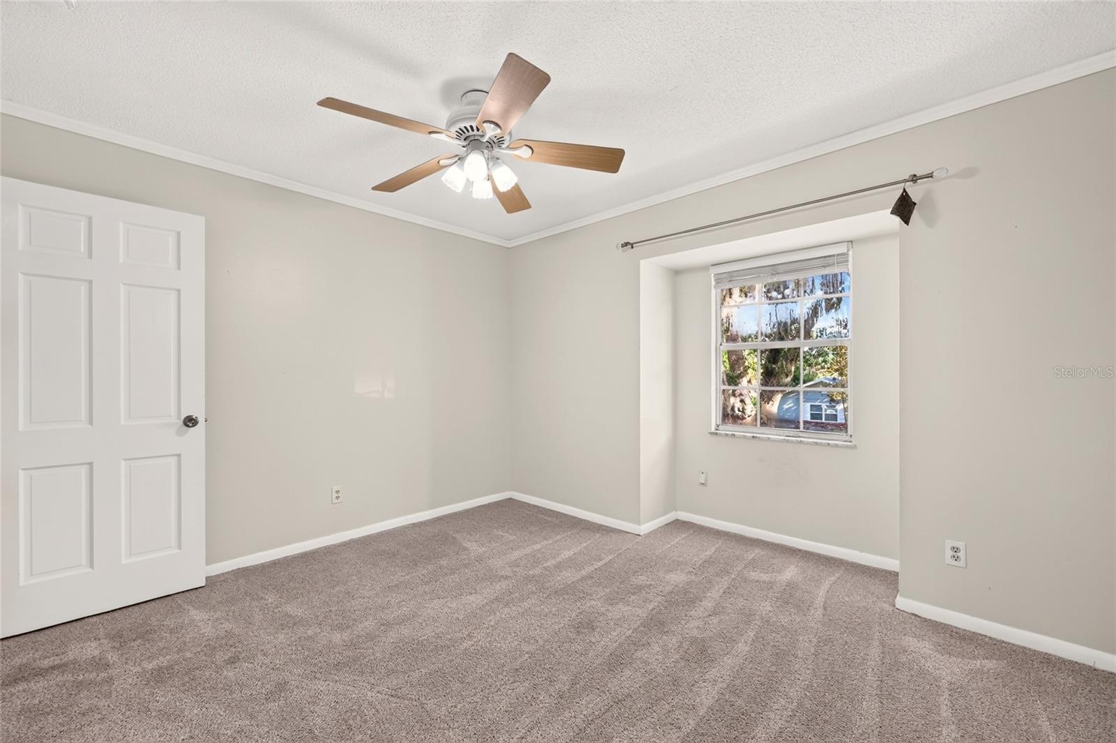 Empty bedroom with beige carpet, a window with blinds, and a wood-blade ceiling fan.