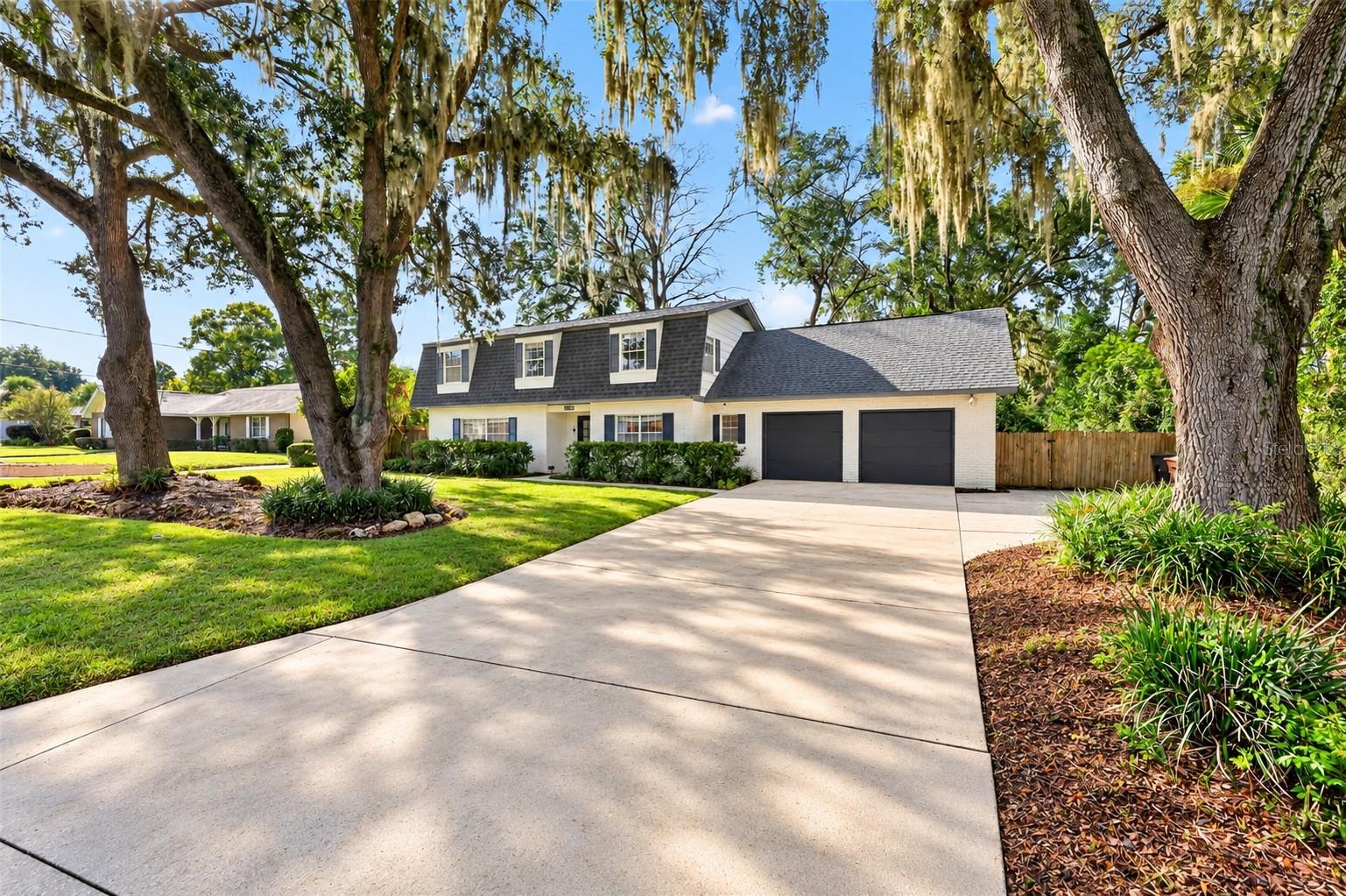White-brick two-story home with a double garage, broad driveway, and moss-draped oak trees.