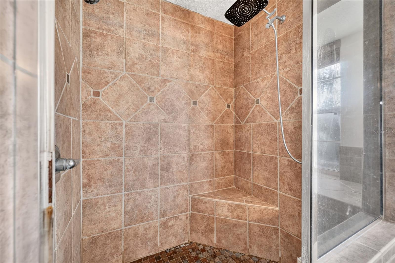 Walk-in shower with warm-toned tile, a corner bench, and overhead rain showerhead.
