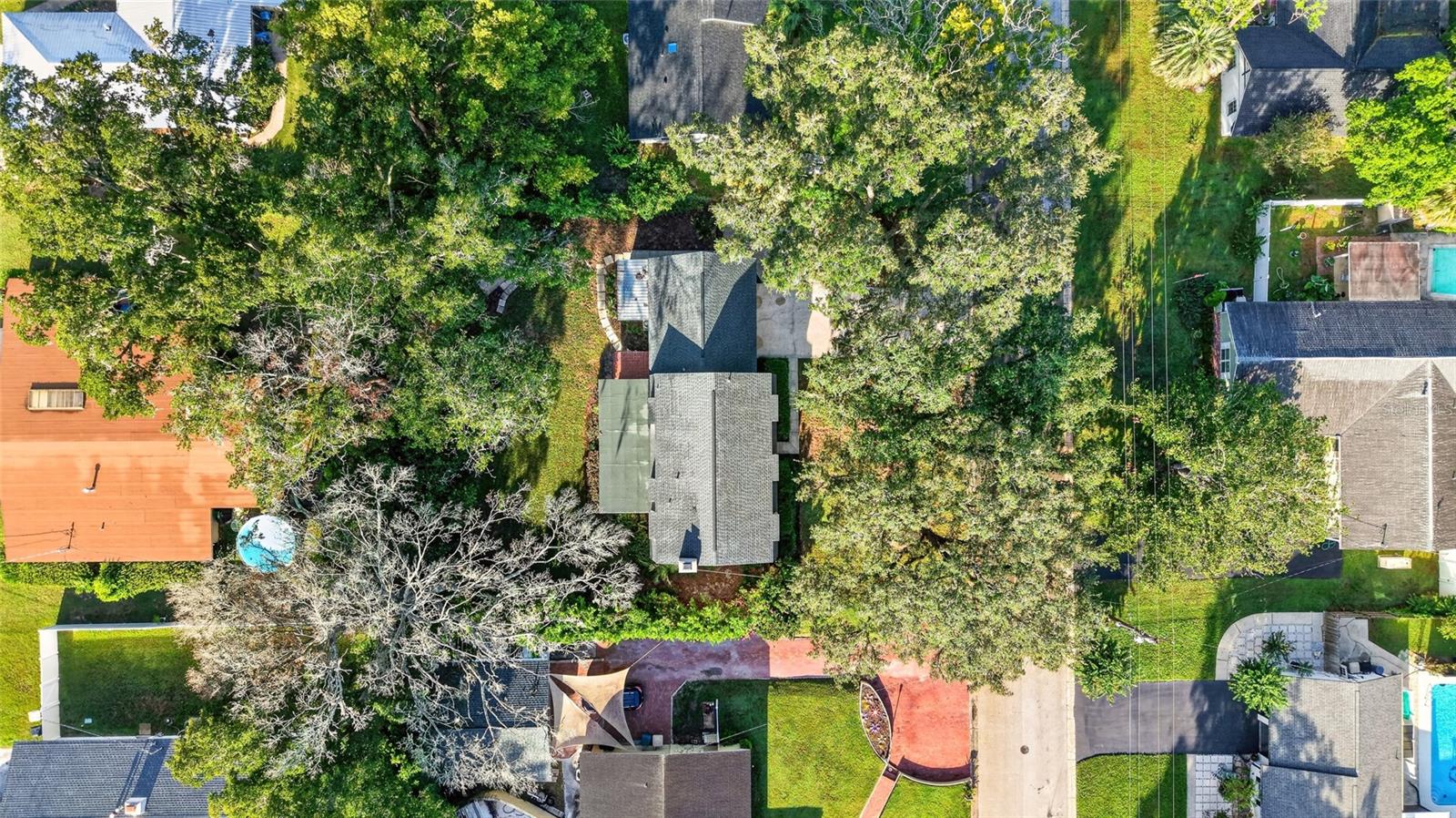 Aerial view of a house on a tree-covered lot among neighboring homes.