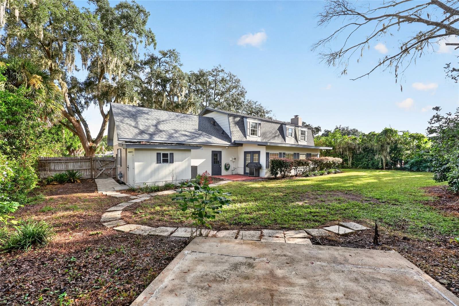Rear of a two-story house with a broad lawn, concrete patio, and mature trees.