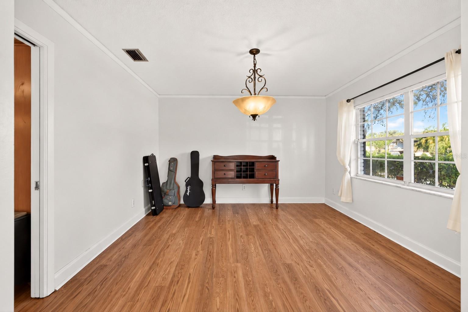 Bright room with wood flooring, a large window, hanging light, and guitar cases beside a console table.
