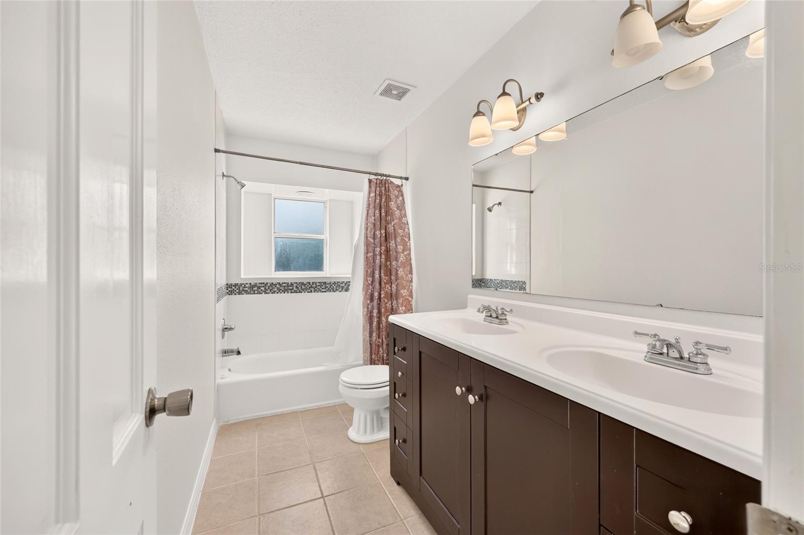 Bathroom with a double-sink vanity and tiled bathtub beneath a window.