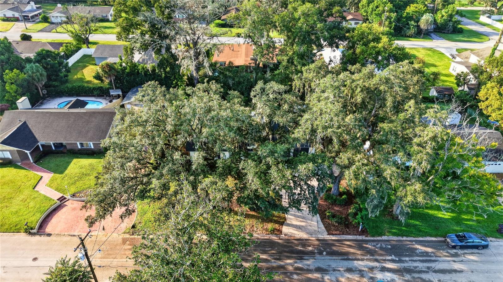 Aerial view of a home largely shaded by mature trees along a residential street.