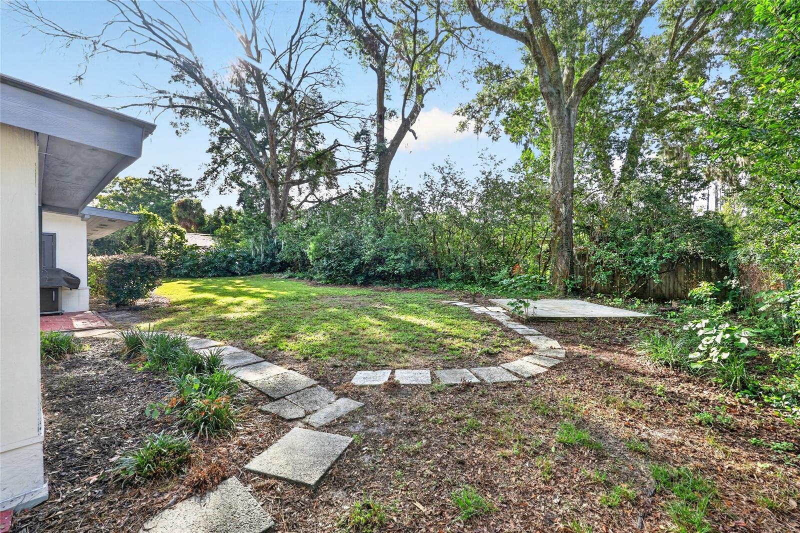 Backyard with a curved stepping-stone path, grassy lawn, mature trees, and dense shrubs.