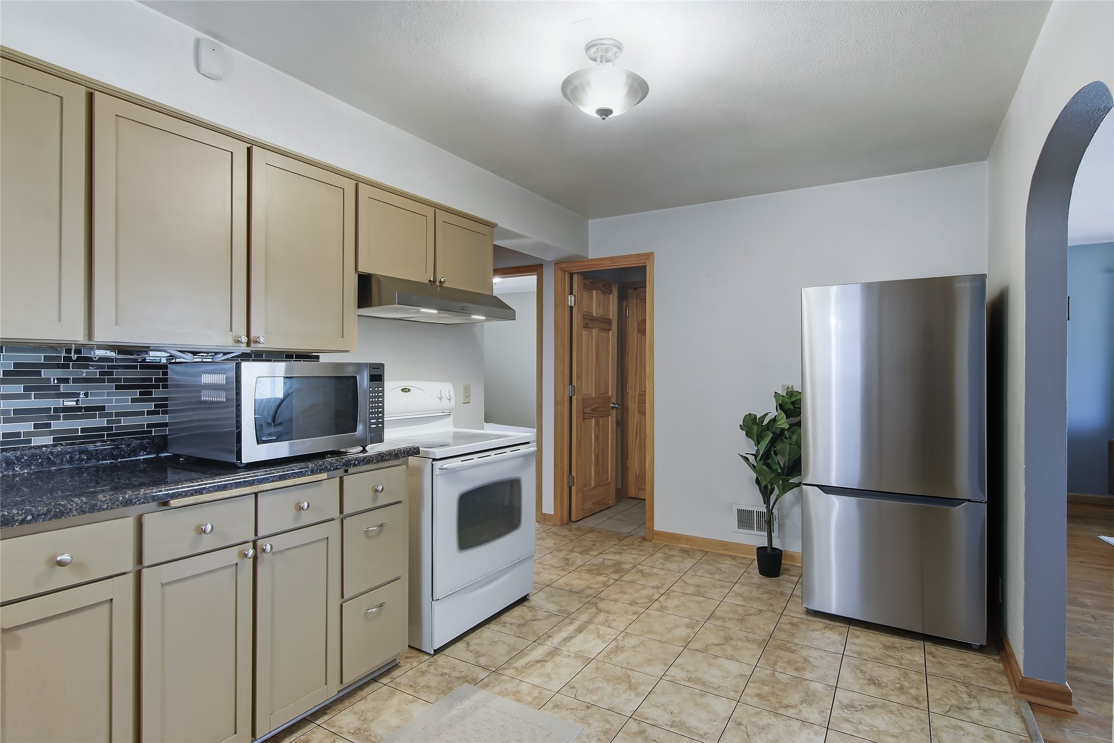 Kitchen with beige cabinets, dark tile backsplash, white stove, and stainless steel refrigerator.