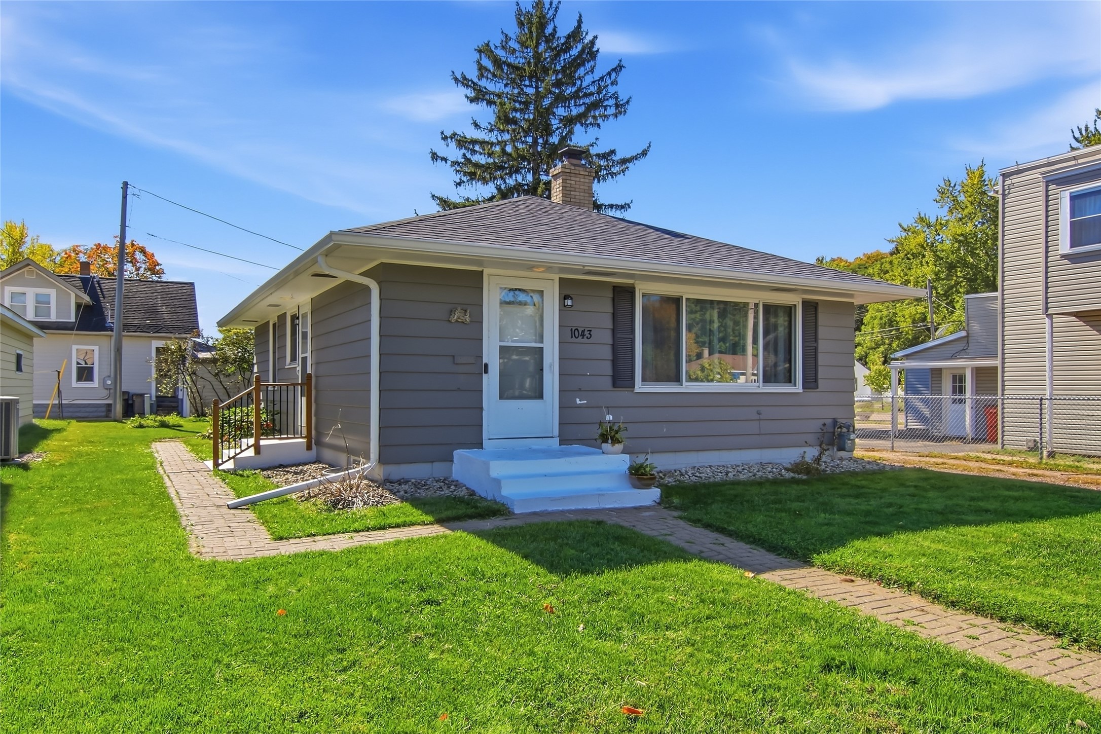 Gray single-story house with white front steps and a brick walkway across the lawn.