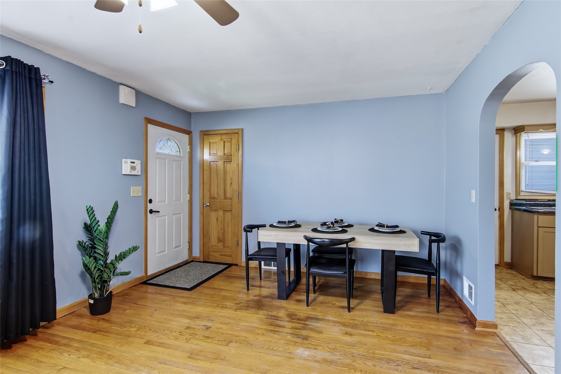 Dining area with a set table, blue walls, hardwood floors, and an arched opening to the kitchen.
