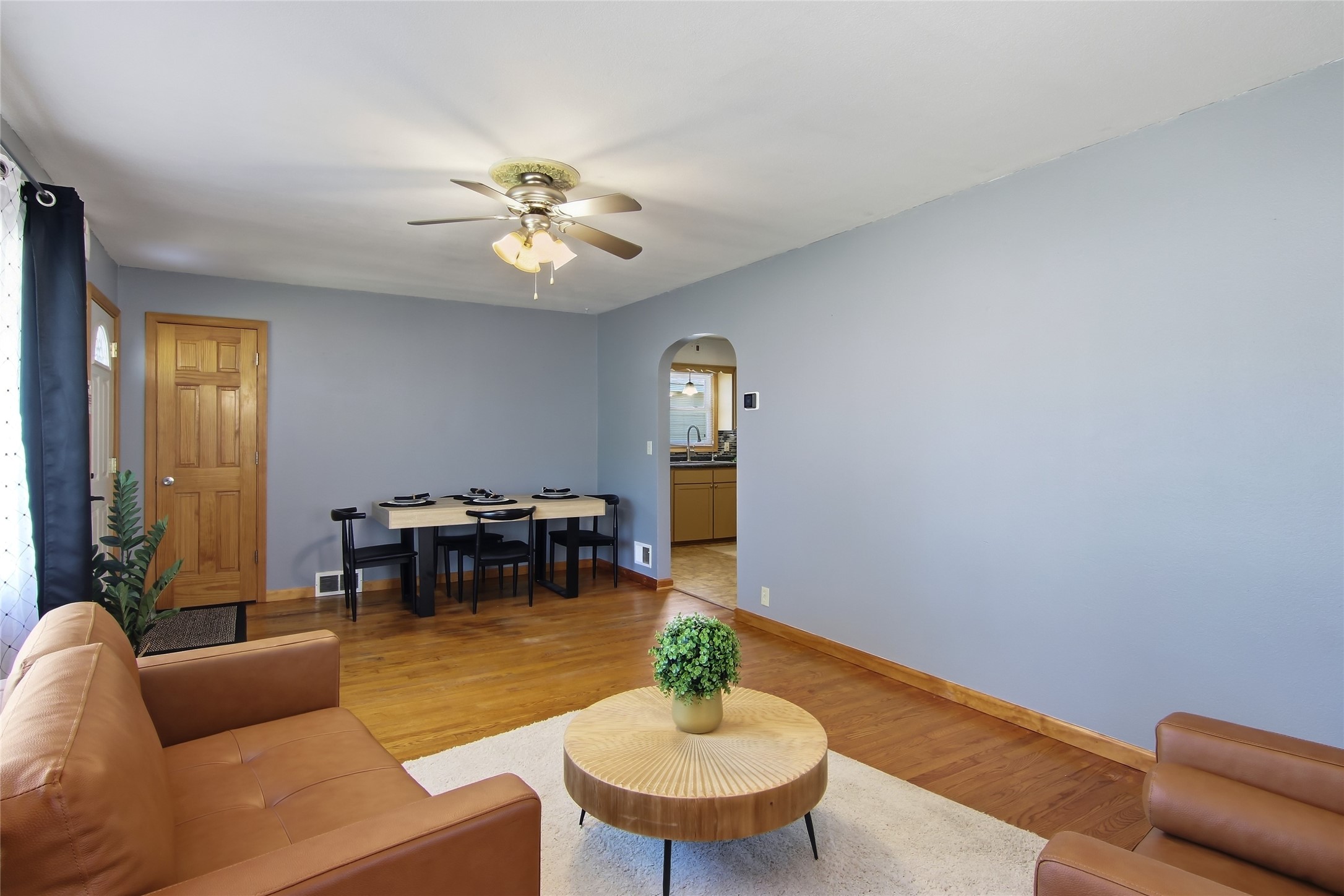 Living and dining room with hardwood floors, leather seating, and an arched opening to the kitchen.