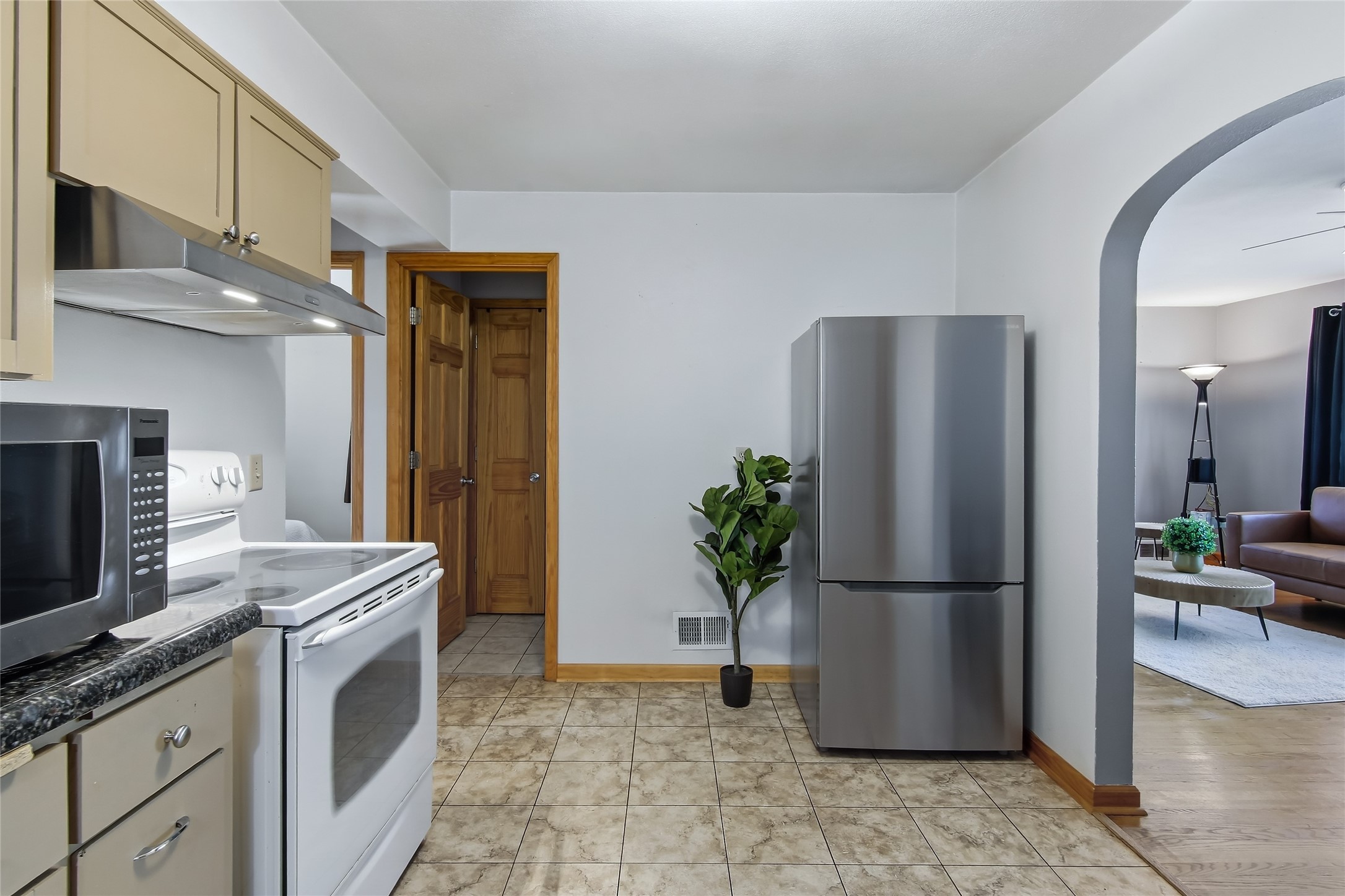 Kitchen with cream cabinets and white range, opening through an archway to the living room.