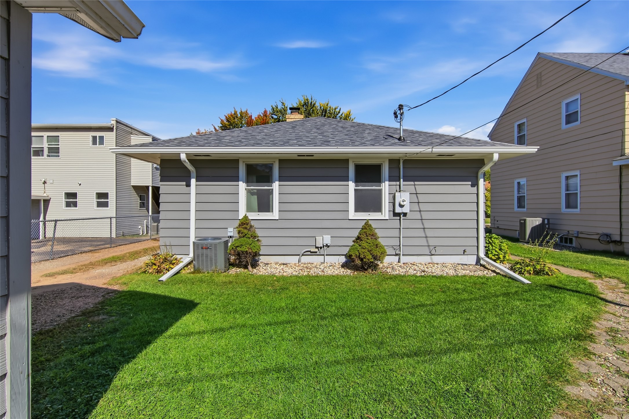 Rear of gray-sided house with two windows and a green lawn.