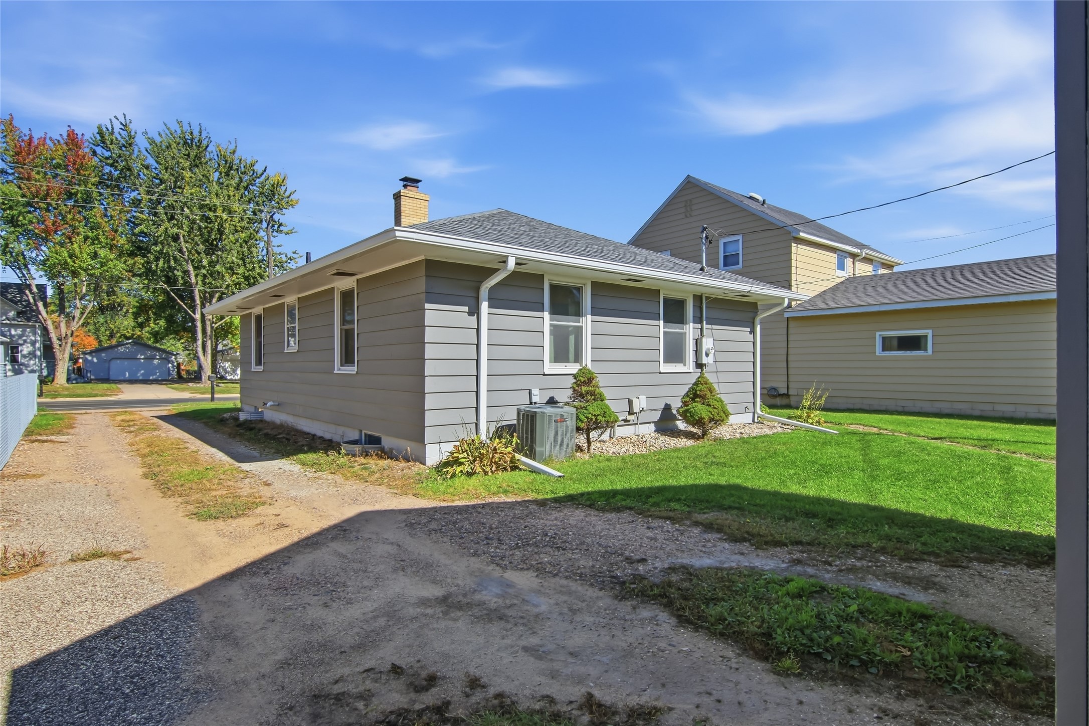 Side exterior of a gray single-story house with a gravel driveway and green lawn.