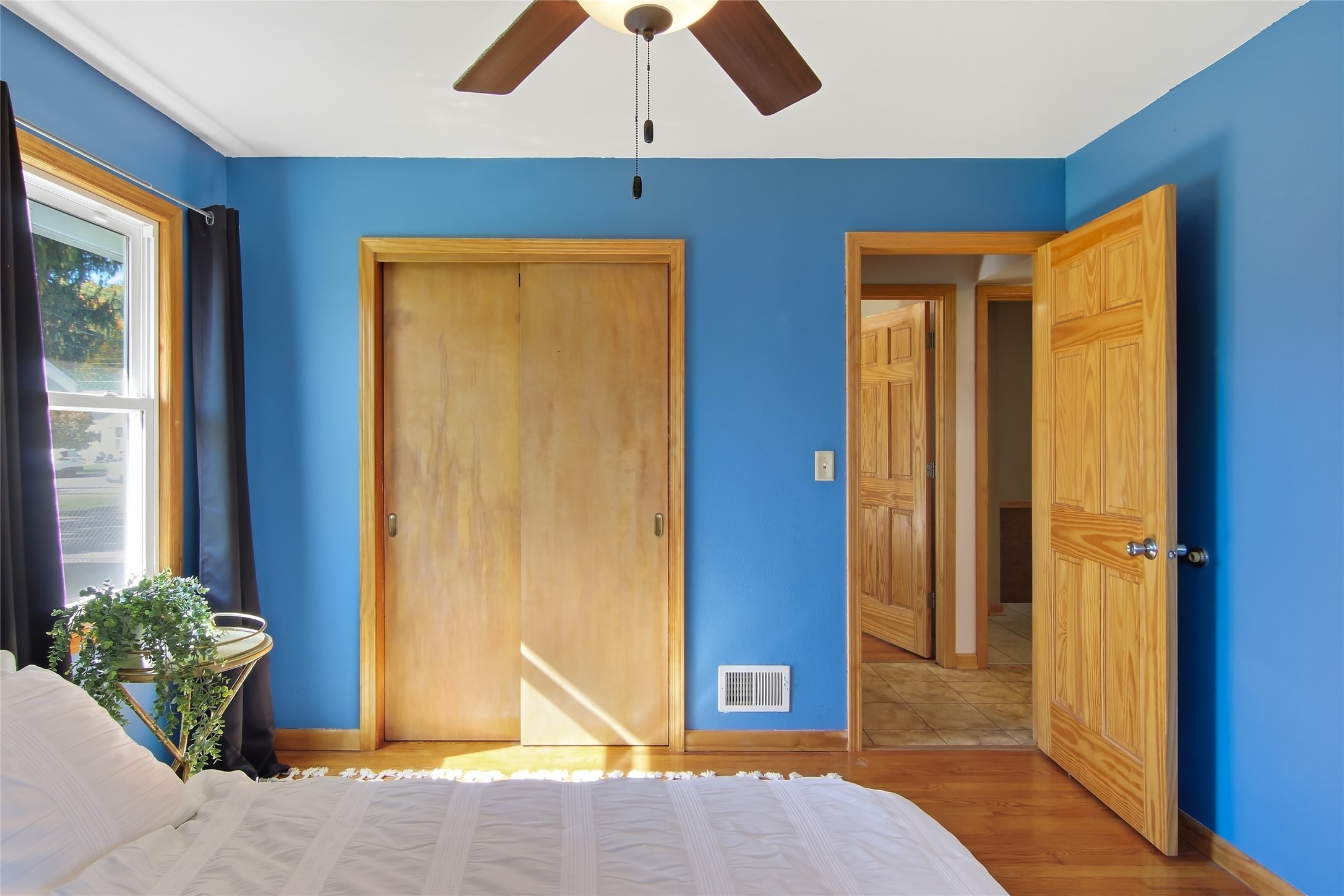 Bedroom with bright blue walls, white bed, wooden closet doors, and an open doorway.
