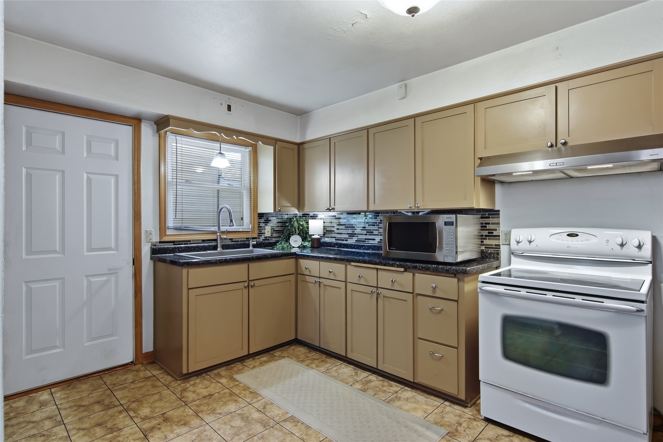Kitchen with tan cabinets, dark countertops, colorful tile backsplash, and a white stove.