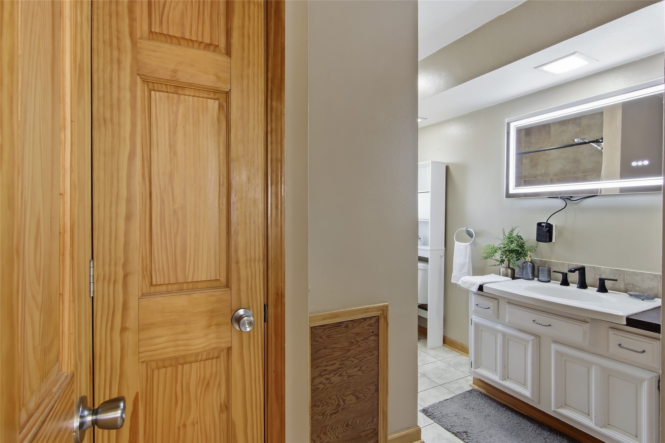 Bathroom with a white double-sink vanity, illuminated mirror, and natural wood doors.