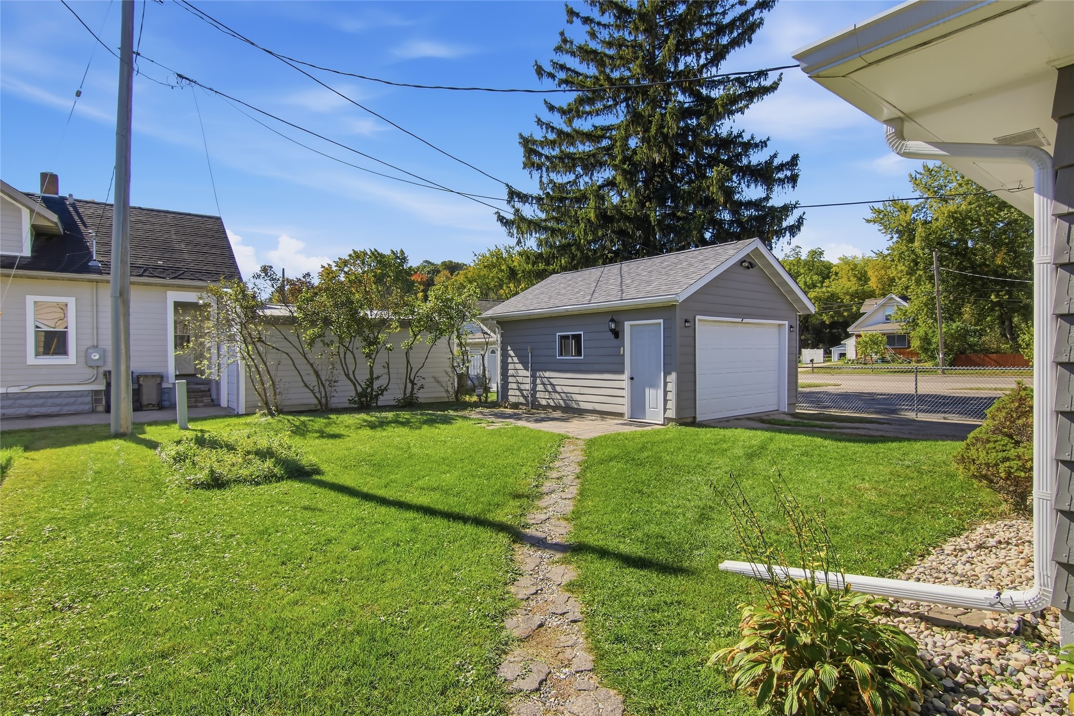 Detached gray garage with white doors beside a stone path and green lawn.