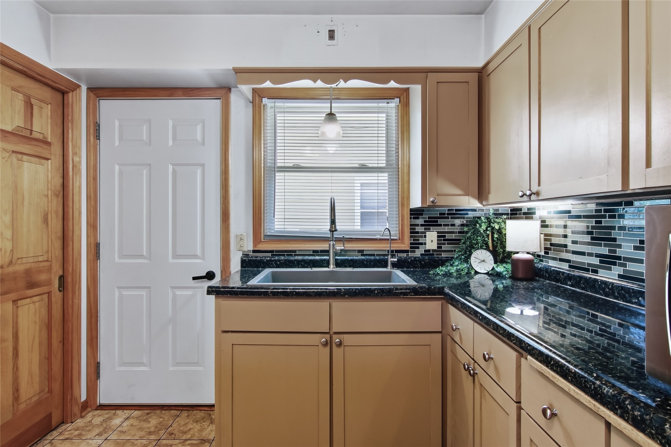Kitchen with tan cabinets, dark stone counters, and a sink beneath a window.