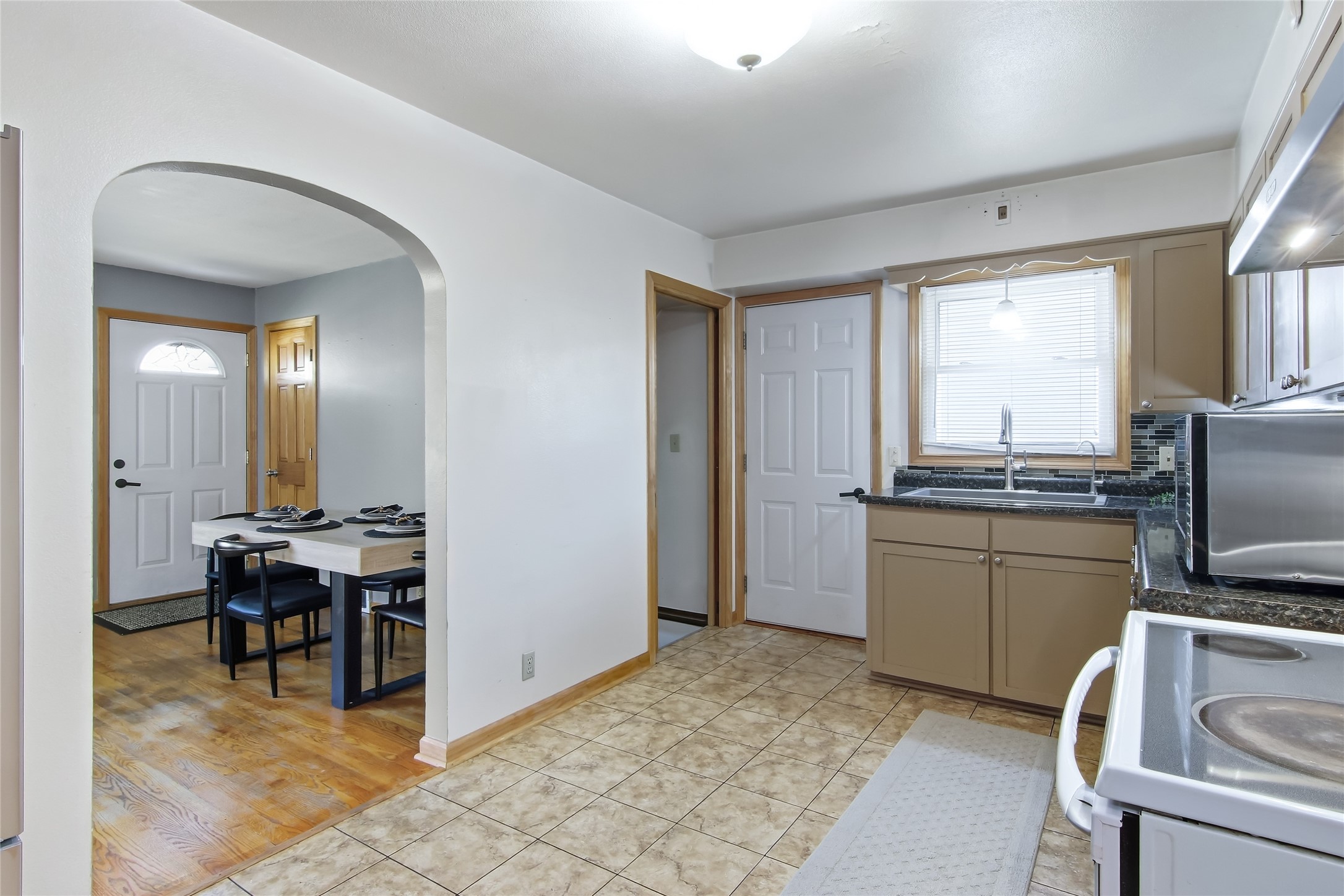 Kitchen with tan cabinets and tiled floor, opening into a dining area with a set table.