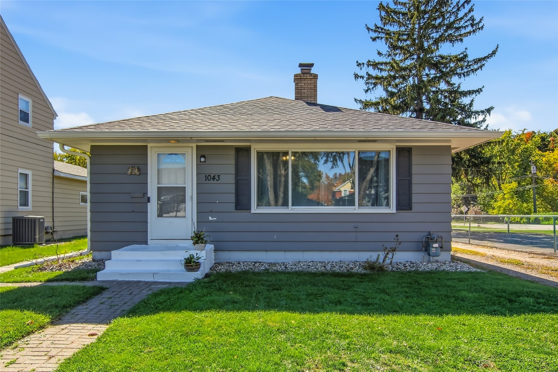 Single-story gray house with white entry steps, a brick chimney, and a green front lawn.