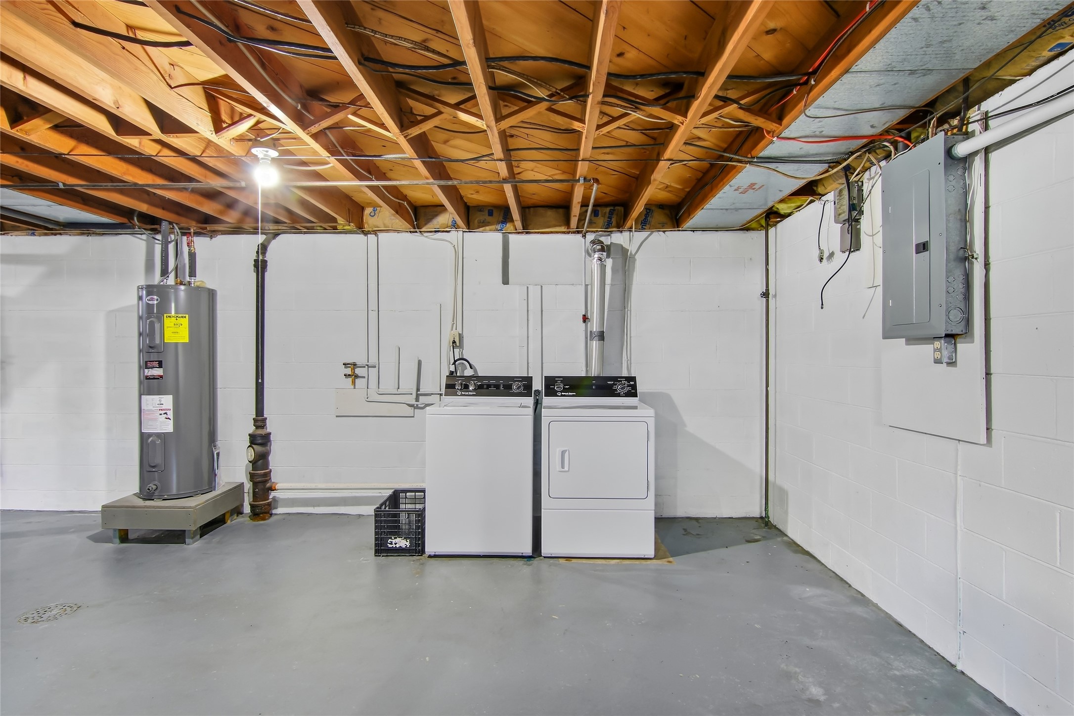 Basement laundry area with washer, dryer, water heater, and exposed ceiling joists.
