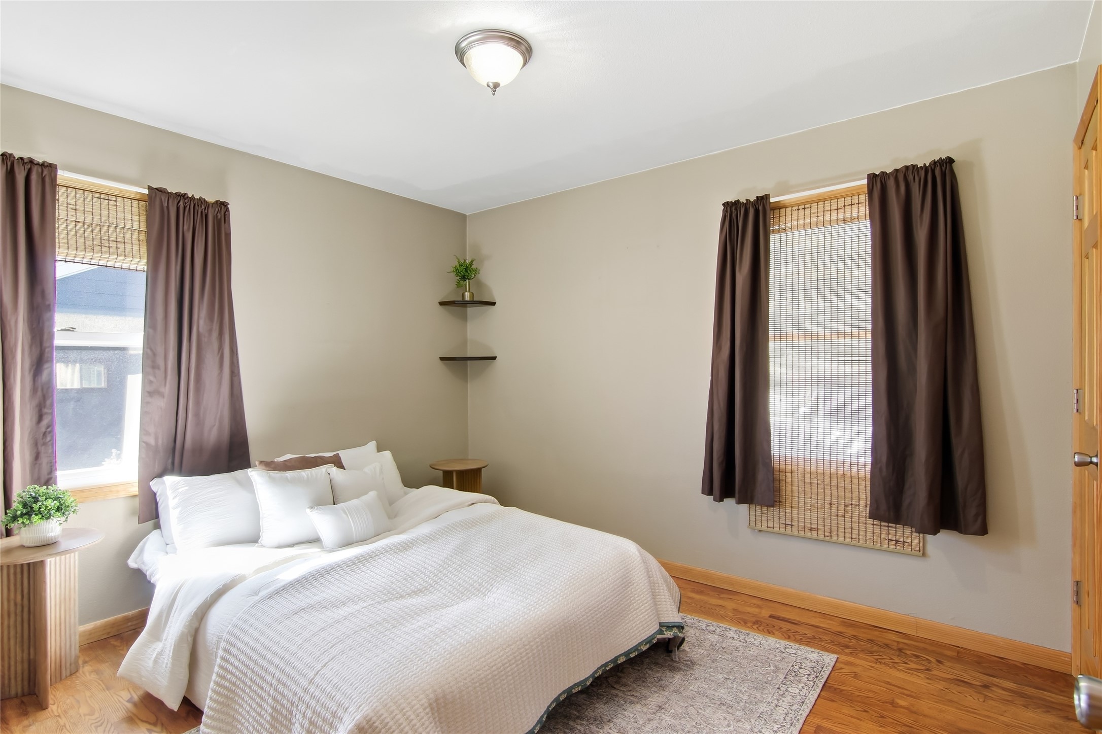 Bedroom with a white quilted bed, hardwood floors, and windows framed by dark curtains.
