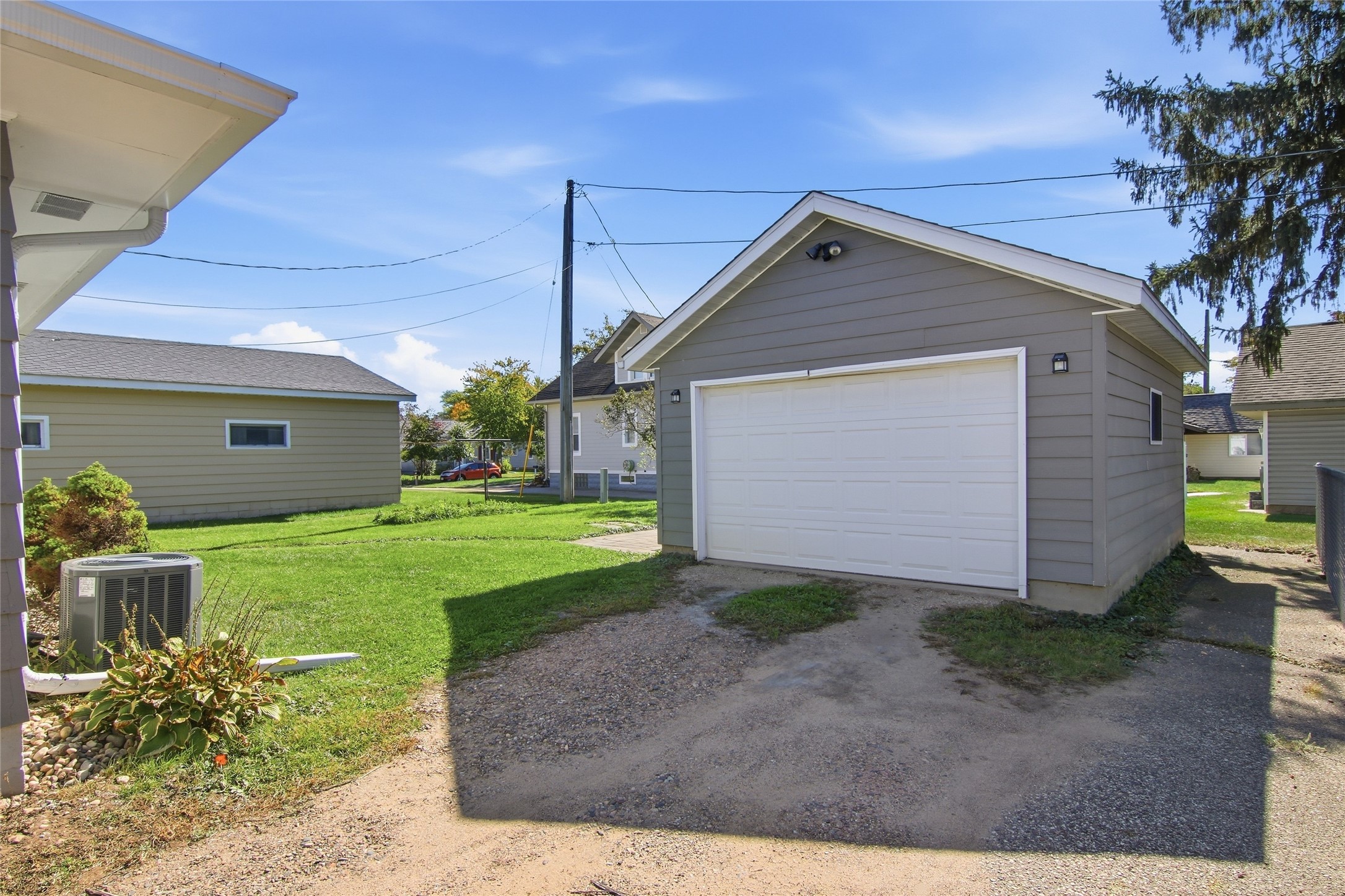 Detached gray garage with a wide white double door and gravel driveway.