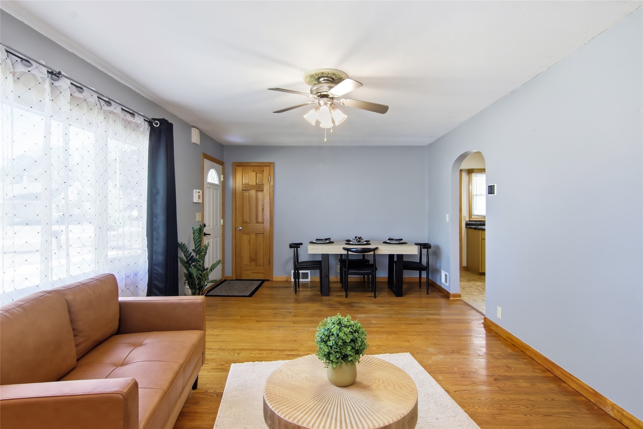 Living and dining area with hardwood floors, a tan leather sofa, and a dining table beside the kitchen opening.