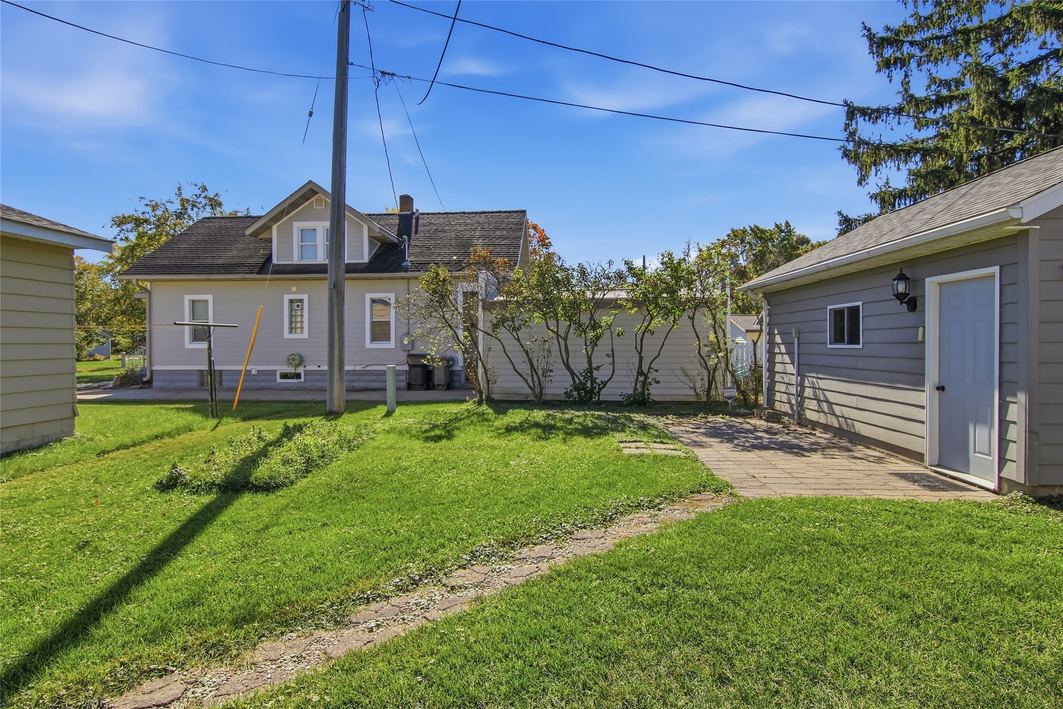 Backyard with a gray house and detached garage beside a paved walkway and lawn.