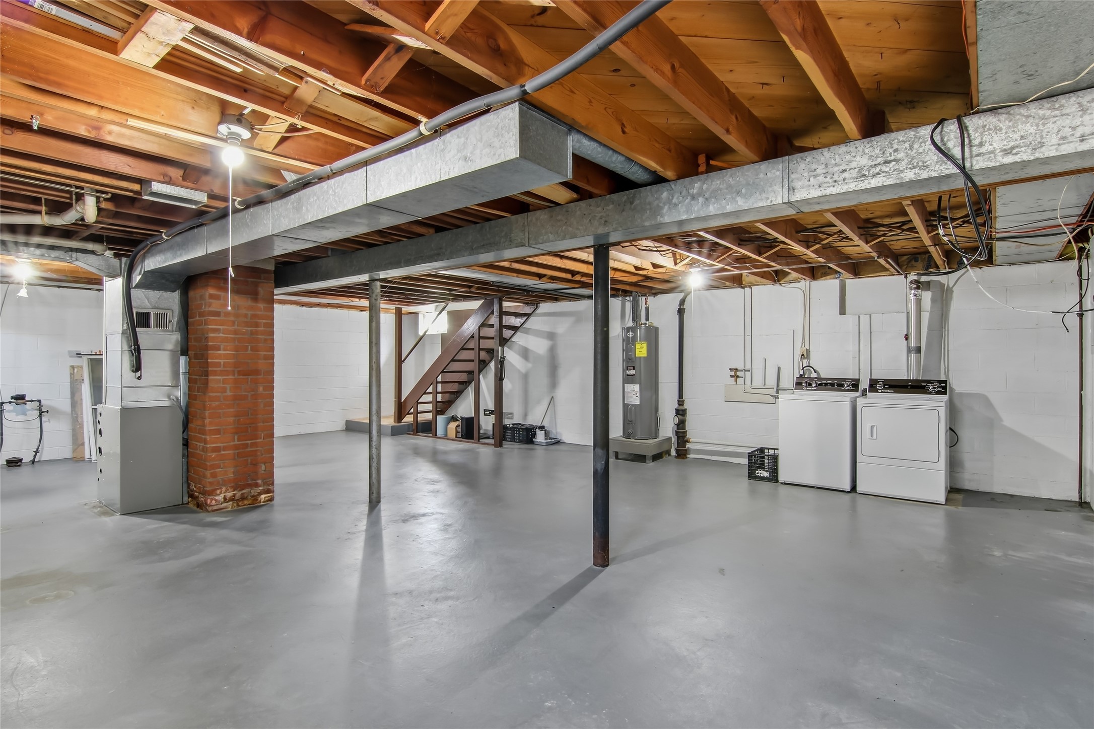 Unfinished basement with exposed ceiling joists, a brick chimney, utility equipment, and laundry appliances.
