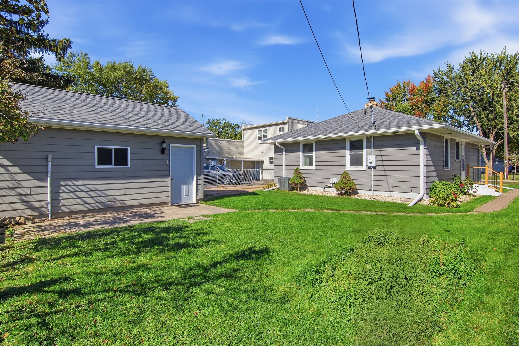 Gray-sided home and separate garage beside a green lawn and mature trees.
