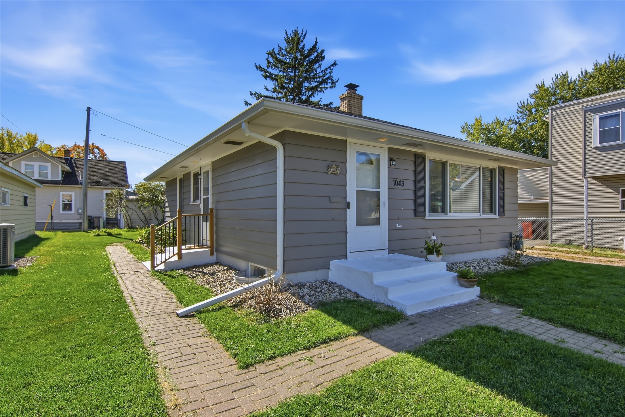 Gray single-story home with white entry steps and a brick walkway across the lawn.