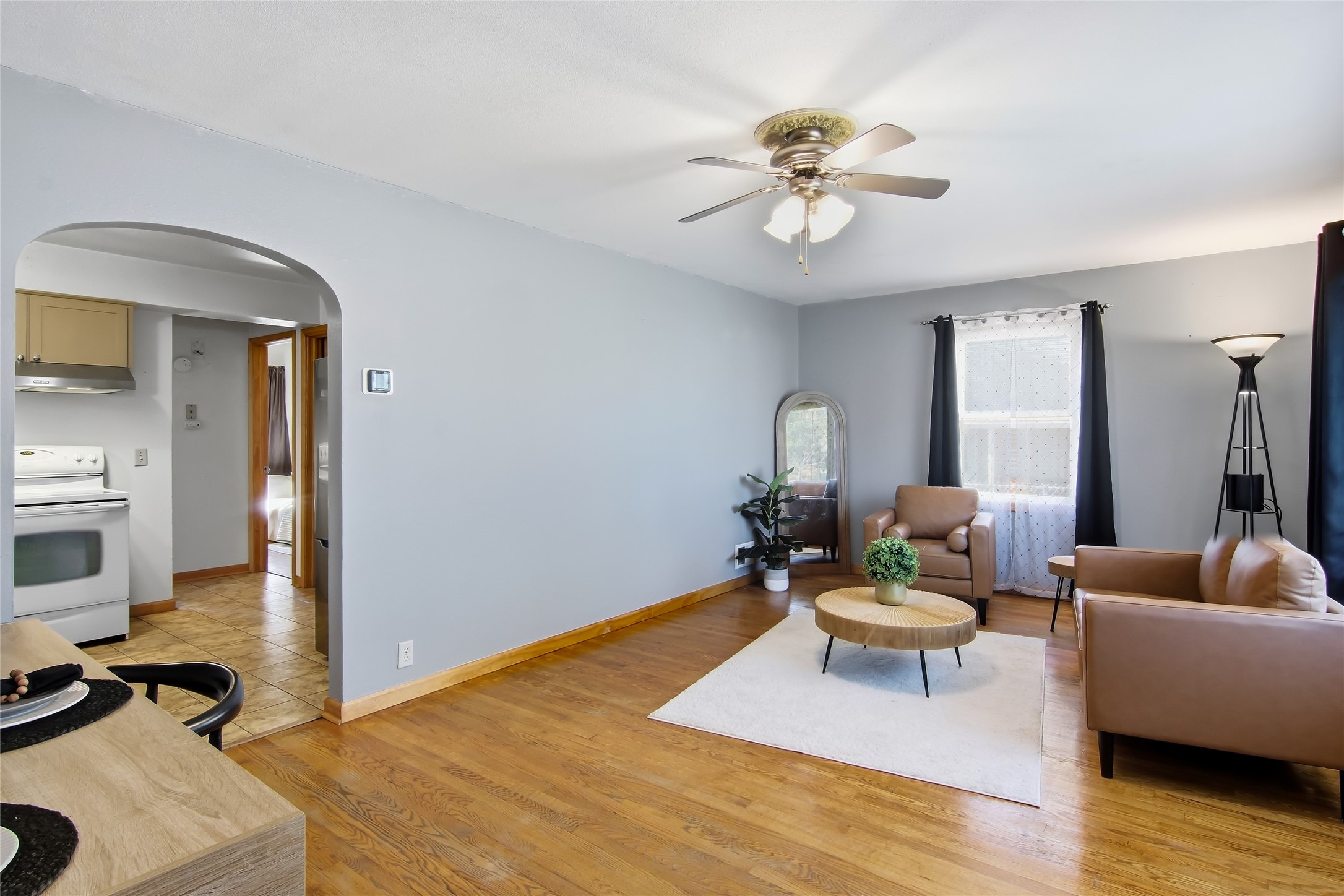 Staged living room with hardwood floors, leather seating, and an arched opening to the kitchen.
