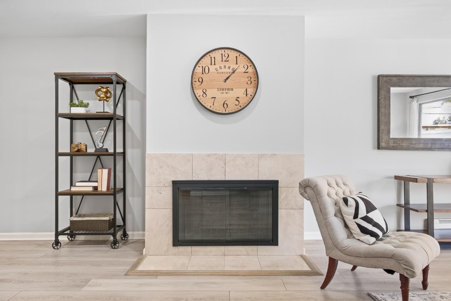 Living room fireplace with pale tile surround, open shelving, and a tufted cream armchair.