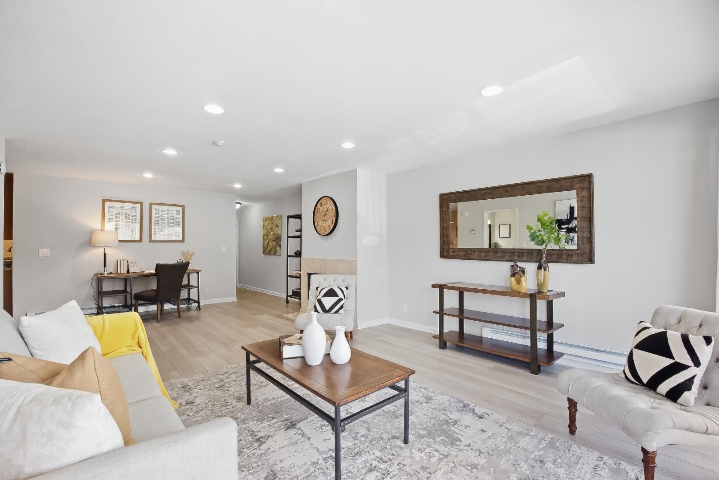 Staged living room with white sofas, a wooden coffee table, and a desk in the back.