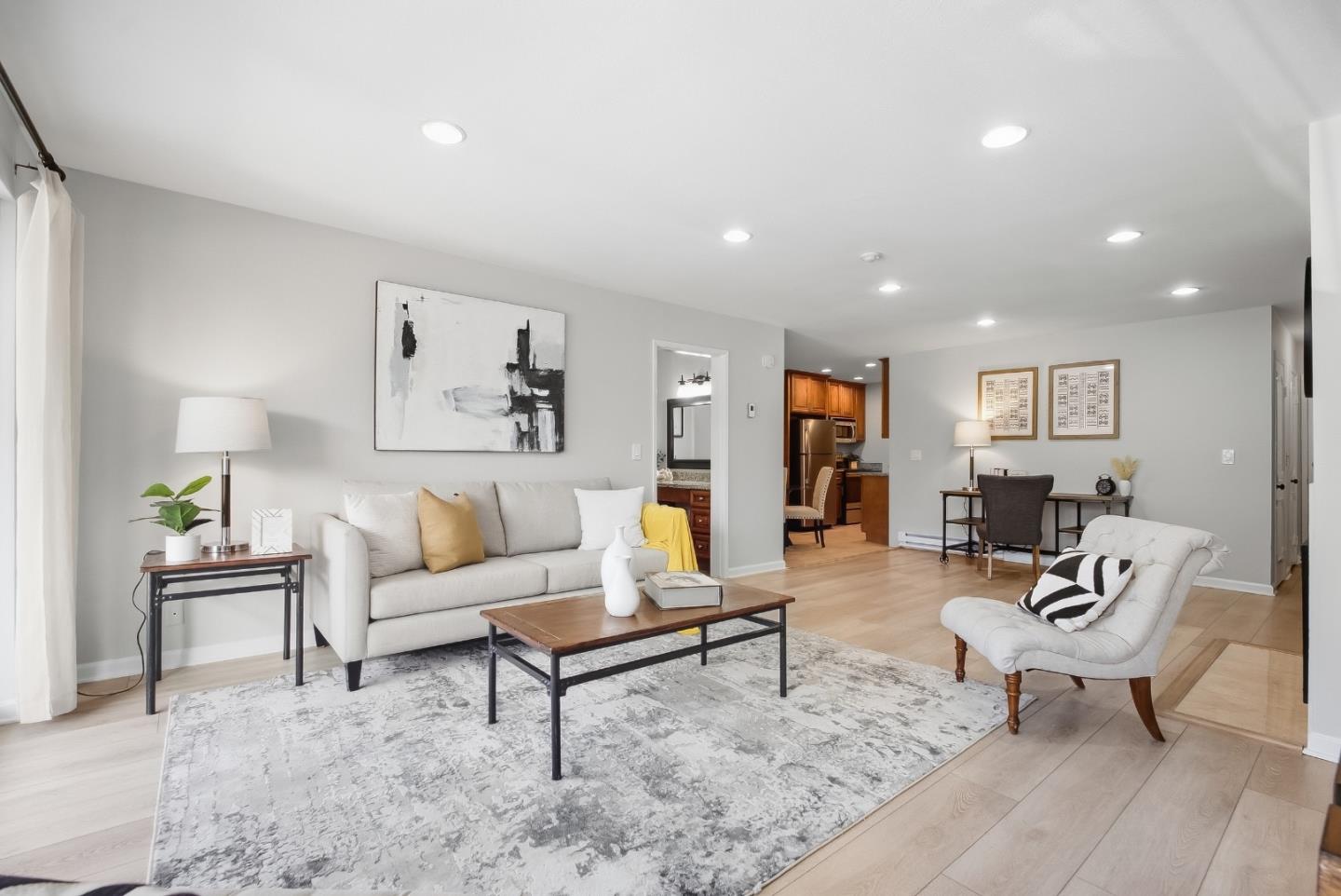 Furnished living room with a white sofa, patterned rug, and open view into the kitchen and dining area.