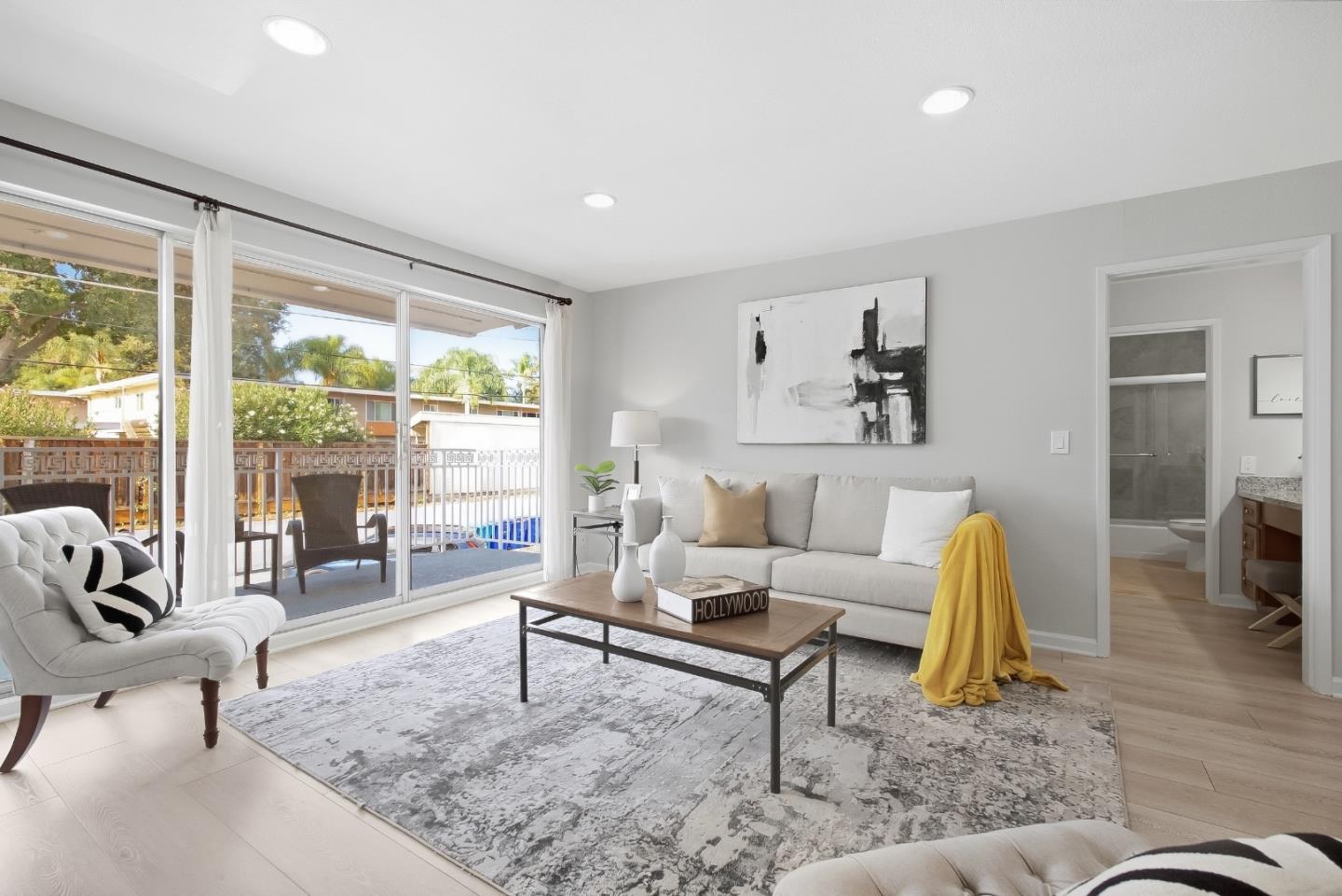Staged living room with white sofas, a patterned rug, and sliding doors opening to a patio.