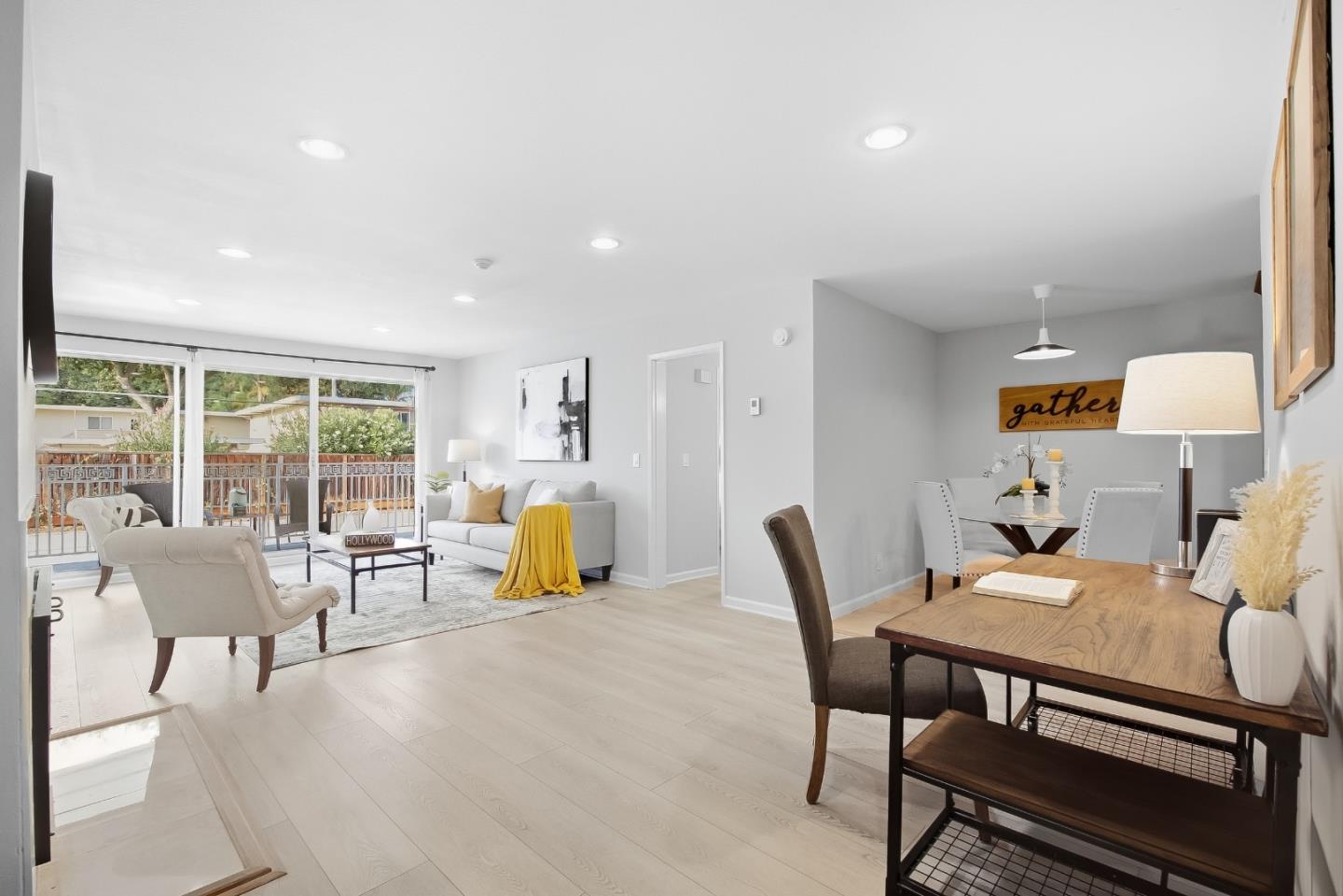 Open-plan living and dining room with pale wood floors, a white sofa, and large sliding glass doors.