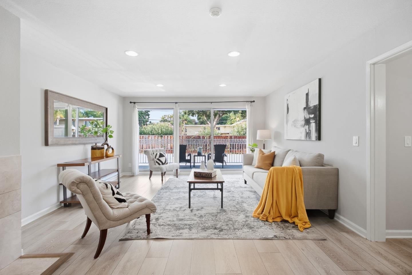 Staged living room with a gray sofa, mustard throw, and sliding doors opening to a balcony.